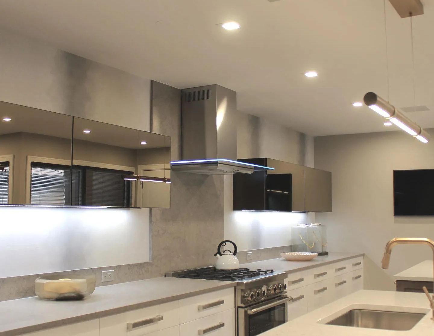Modern kitchen with stainless steel appliances, light cabinets, and a long rectangular light fixture.