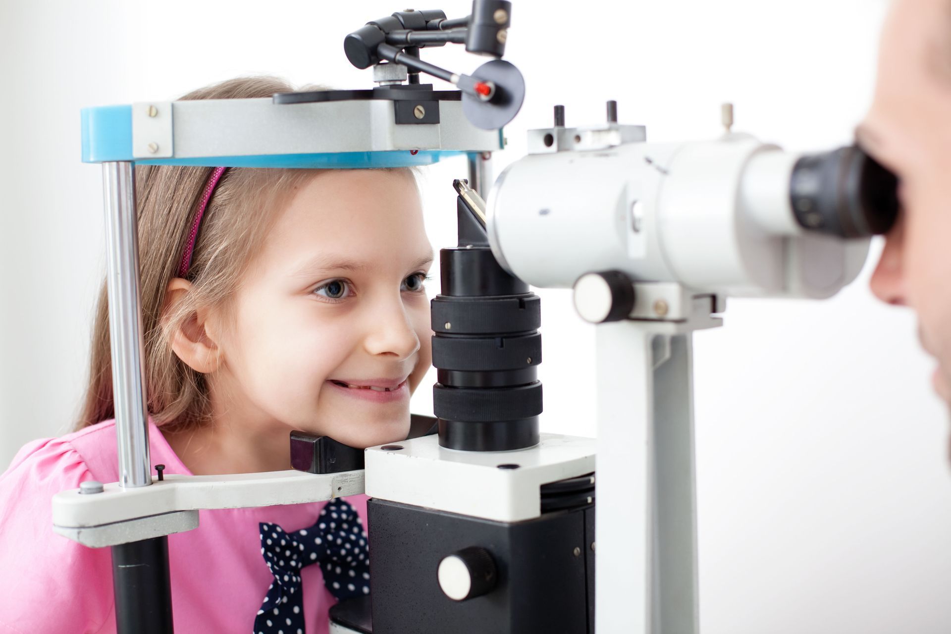 Young girl smiling during eye exam with an eye doctor and a slit lamp.