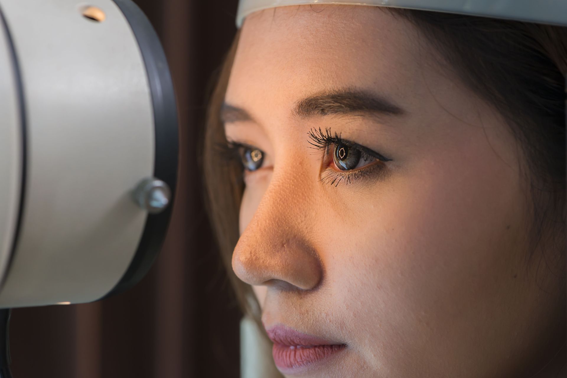 Woman undergoing an eye exam, looking toward an ophthalmic device in a doctor's office.