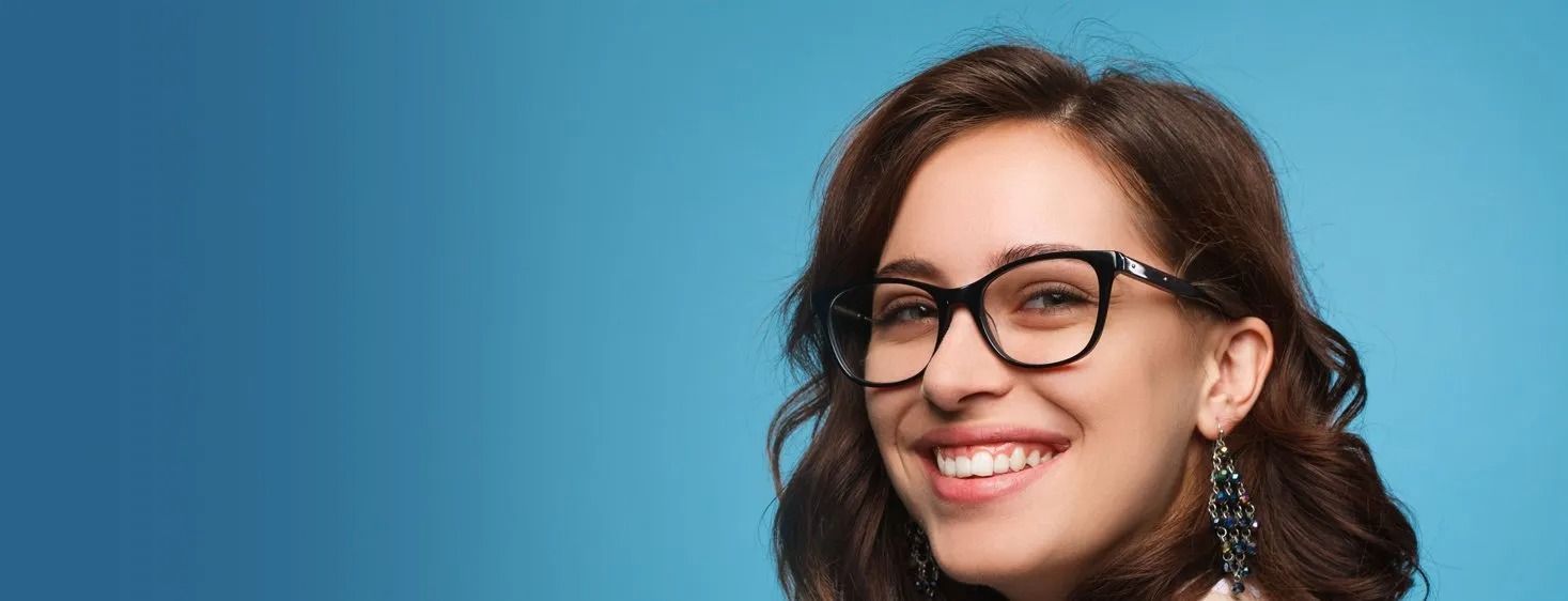 Woman smiling, wearing black glasses, against a blue background.