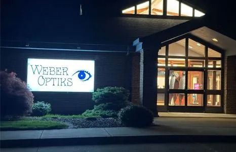 Weber Optiks sign at night. Illuminated storefront with large eye graphic.