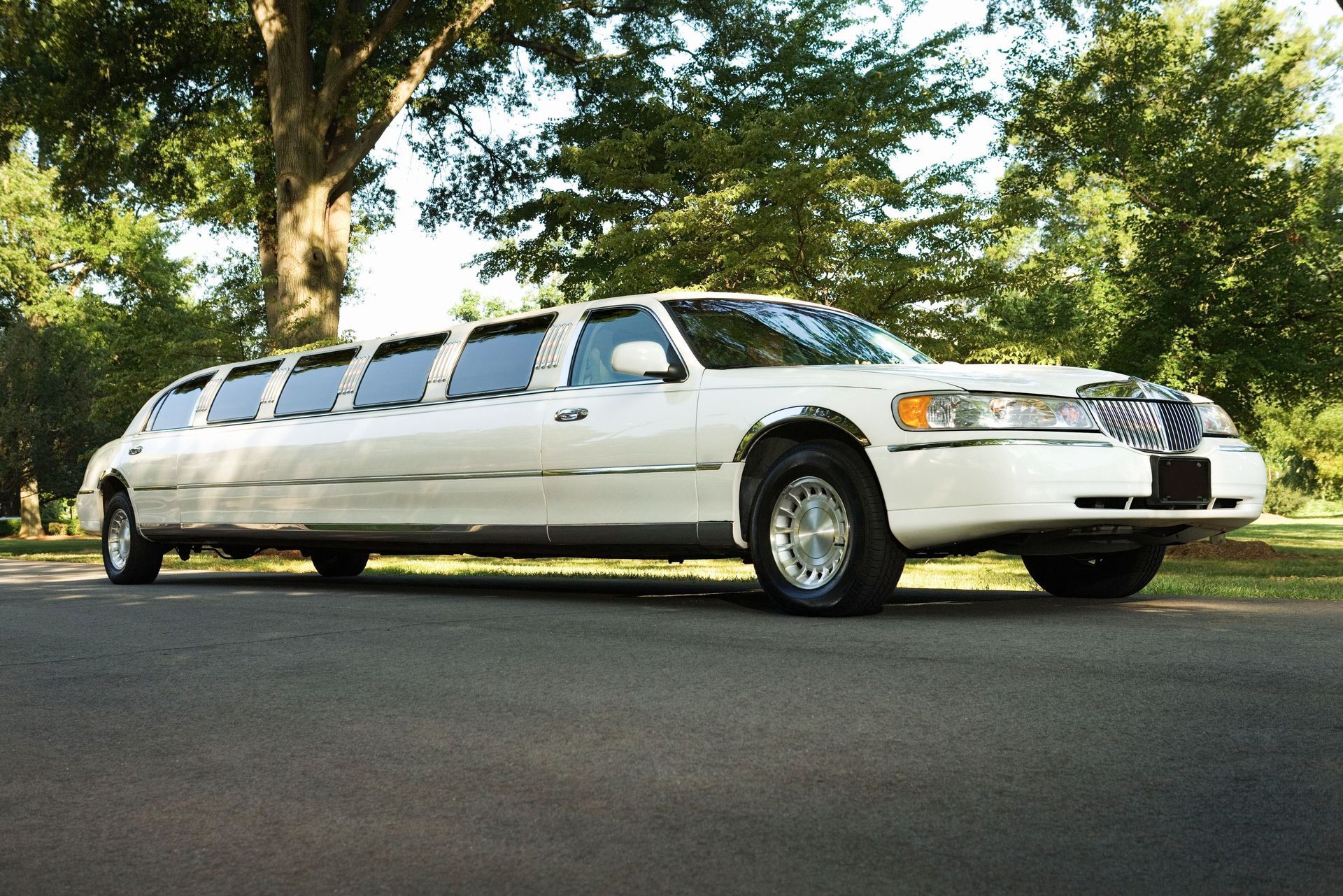 White limousine parked on a paved road, trees in the background.