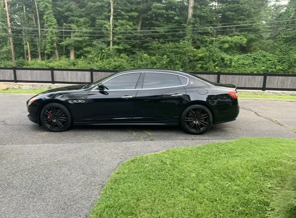 Black Maserati sedan parked on asphalt next to a grassy lawn.
