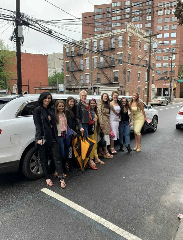 Group of people posing by a white limousine on a city street; overcast day.
