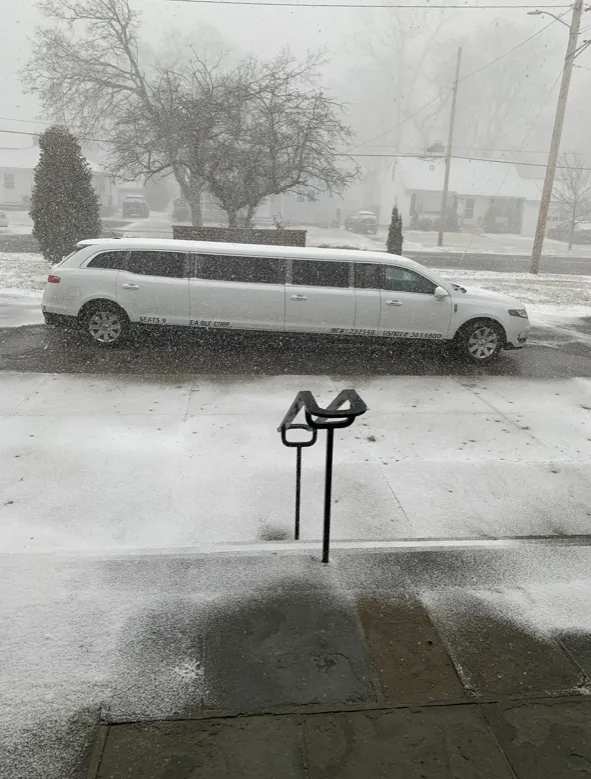 White limousine in a snowstorm, parked on a street. Snow is falling.