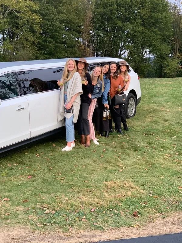 Seven people stand next to a white limousine on a grassy lawn.