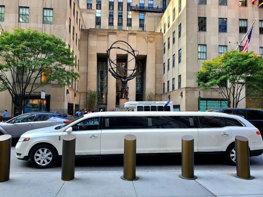 White limousine in front of the Rockefeller Center, New York, with Atlas statue visible.