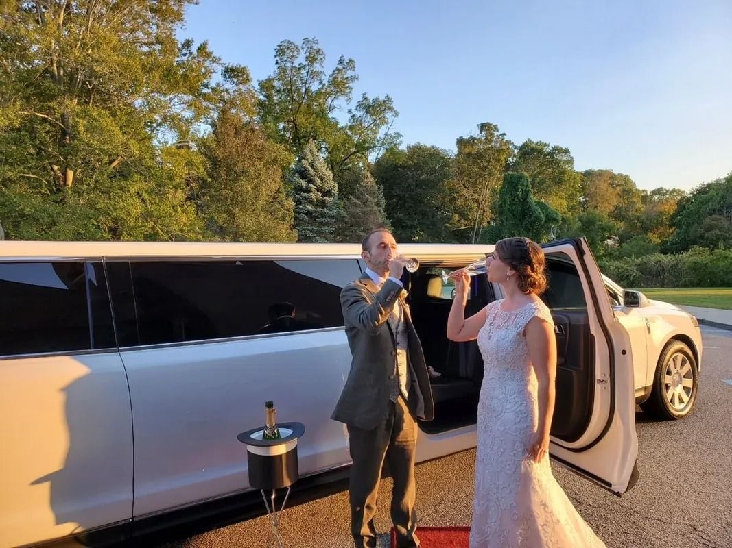 Newlyweds toasting champagne next to a white limousine with open door. Outdoors, sunny day.