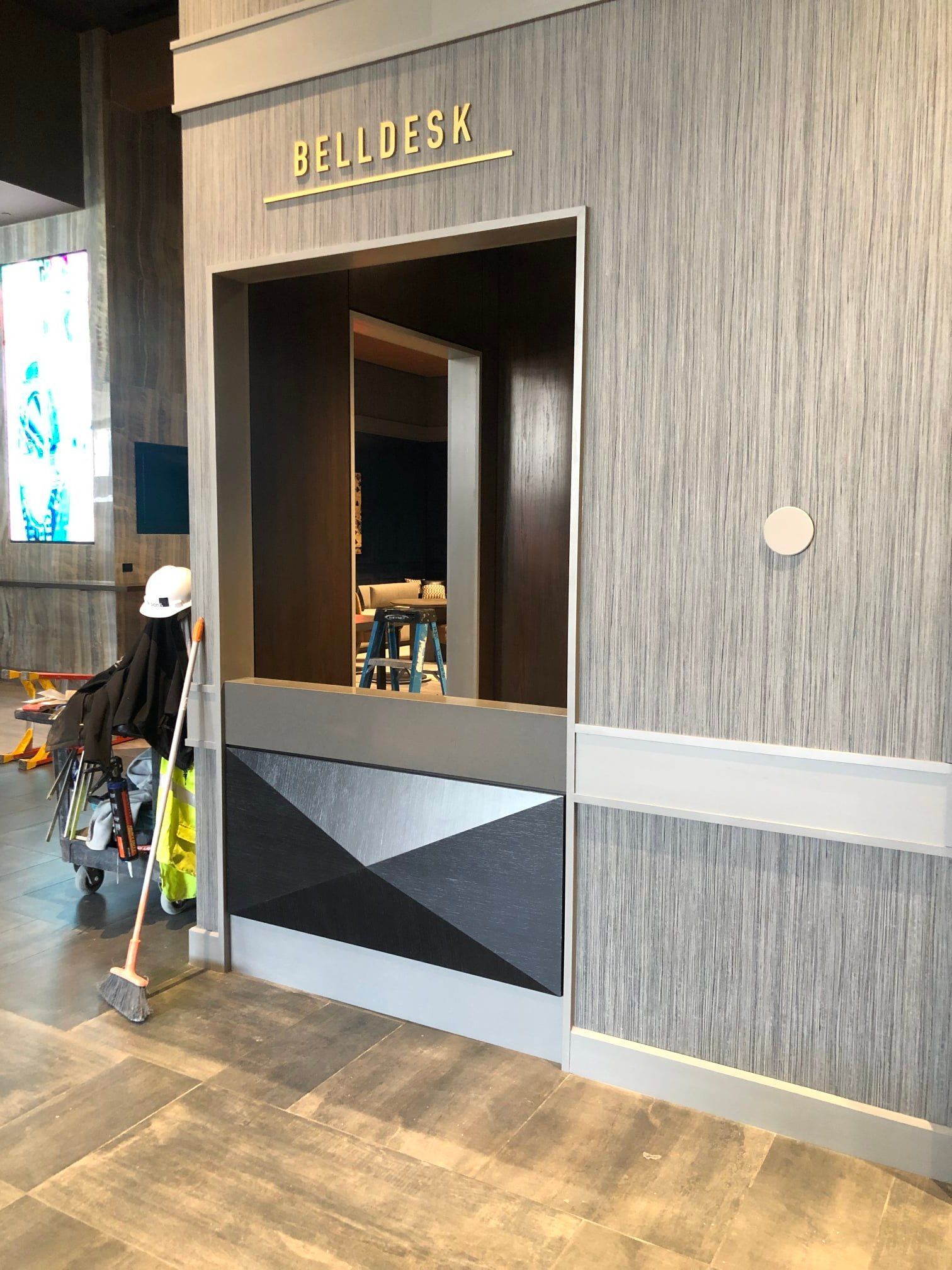 Bell desk with gray wood paneling and geometric pattern, a worker nearby.