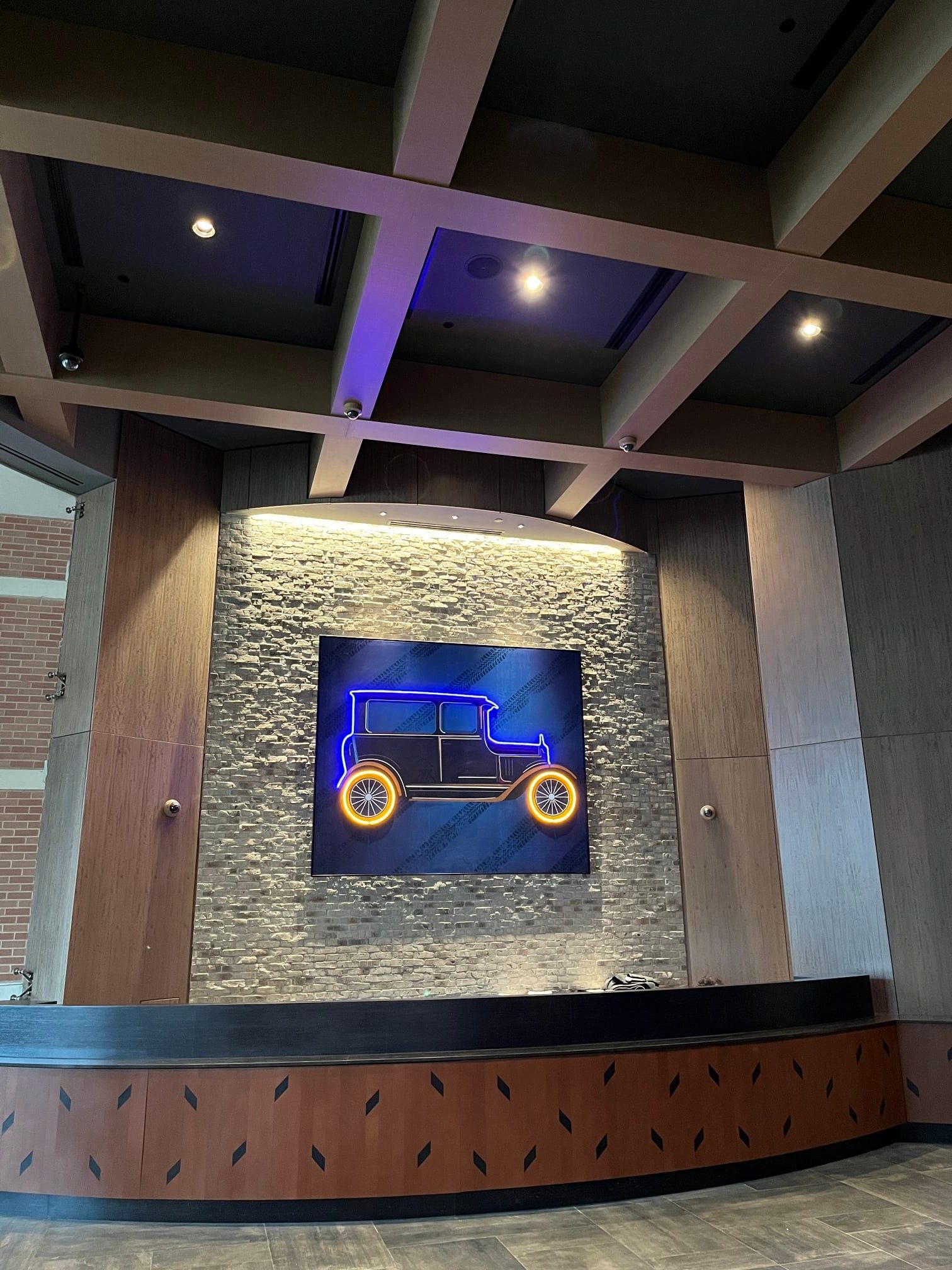 Neon car art on textured wall, above a wooden counter, under a beamed ceiling.