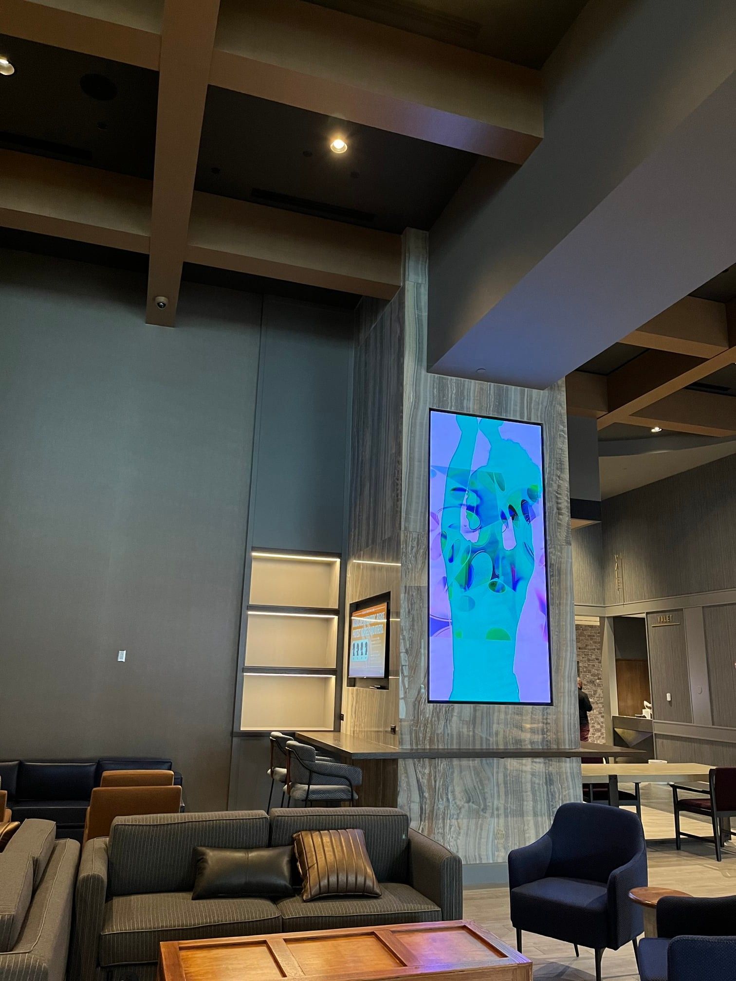 Lounge area with gray walls, sofa, and large digital display showing an abstract image.