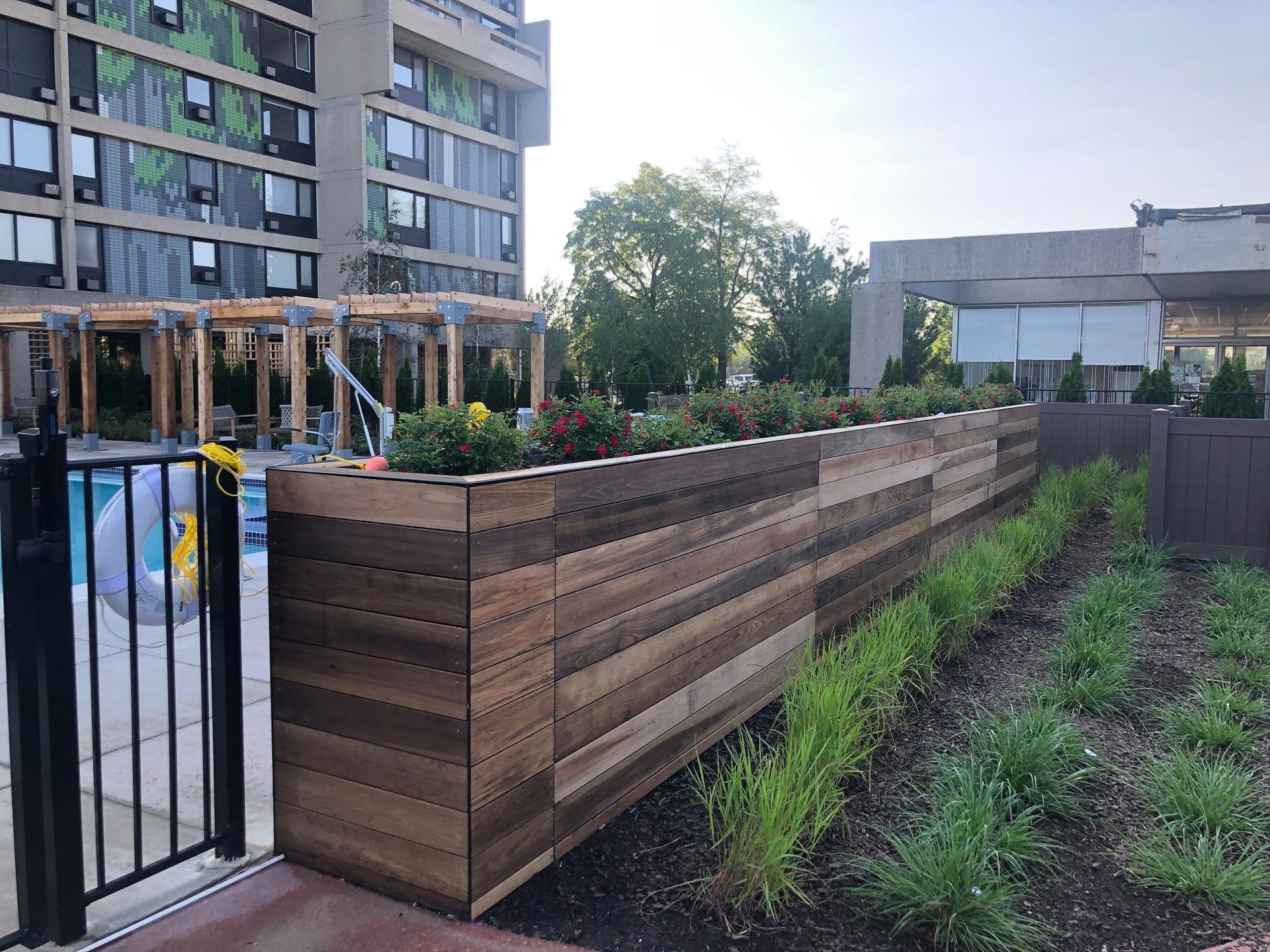 Wooden planter box with flowers, beside a pool with a building in the background.