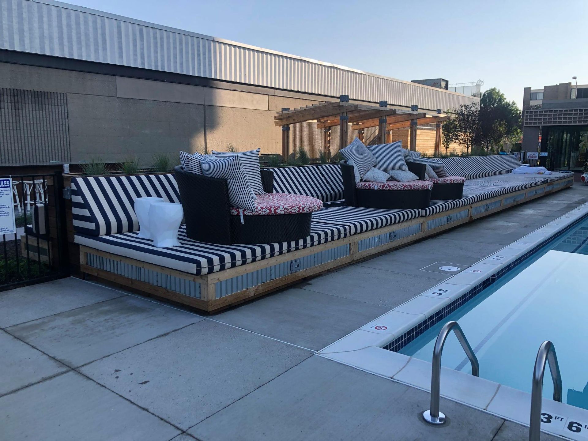 Poolside seating with black and white striped cushions, near a pool, under a building.