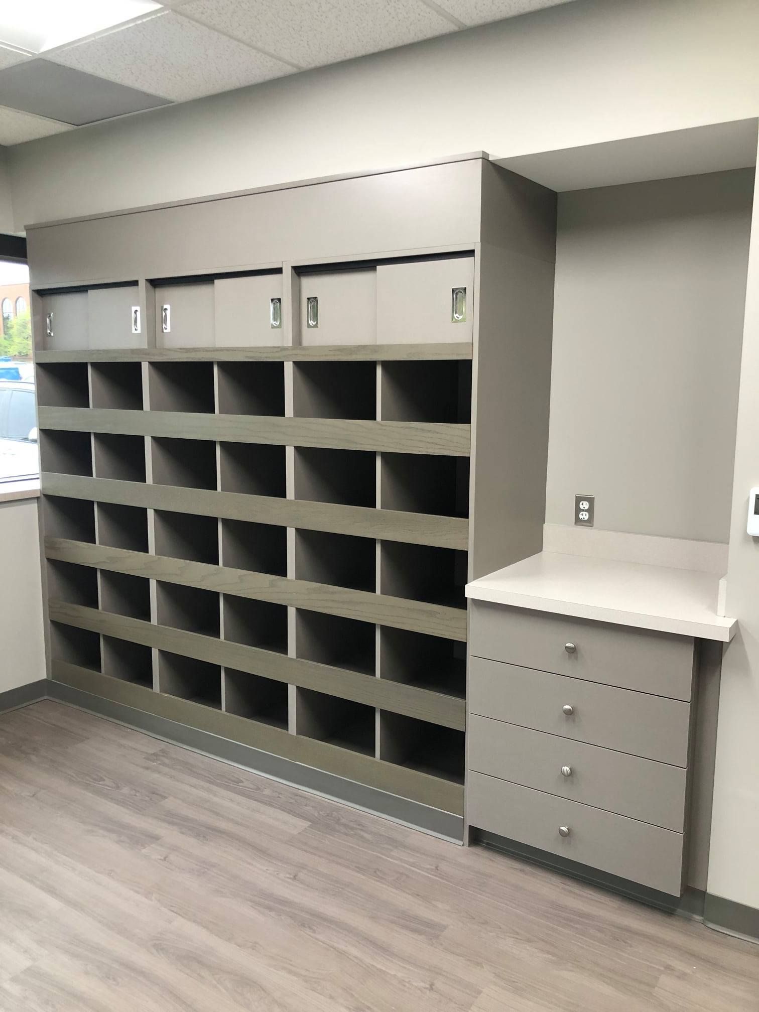 Gray cubby shelves and drawers built into a wall in a room with light-colored flooring and walls.