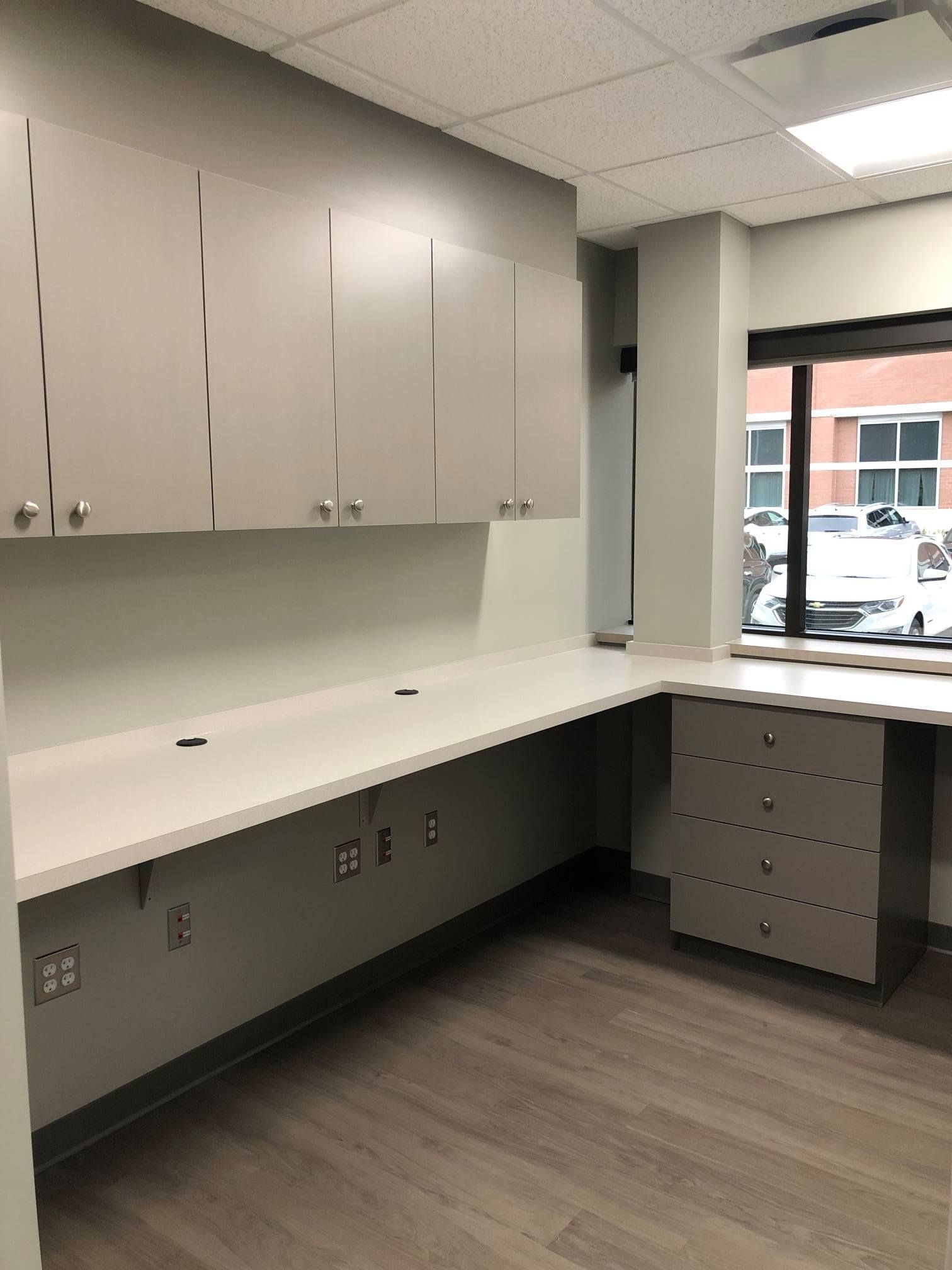 Gray cabinetry and countertop in a corner office with a window overlooking a street.