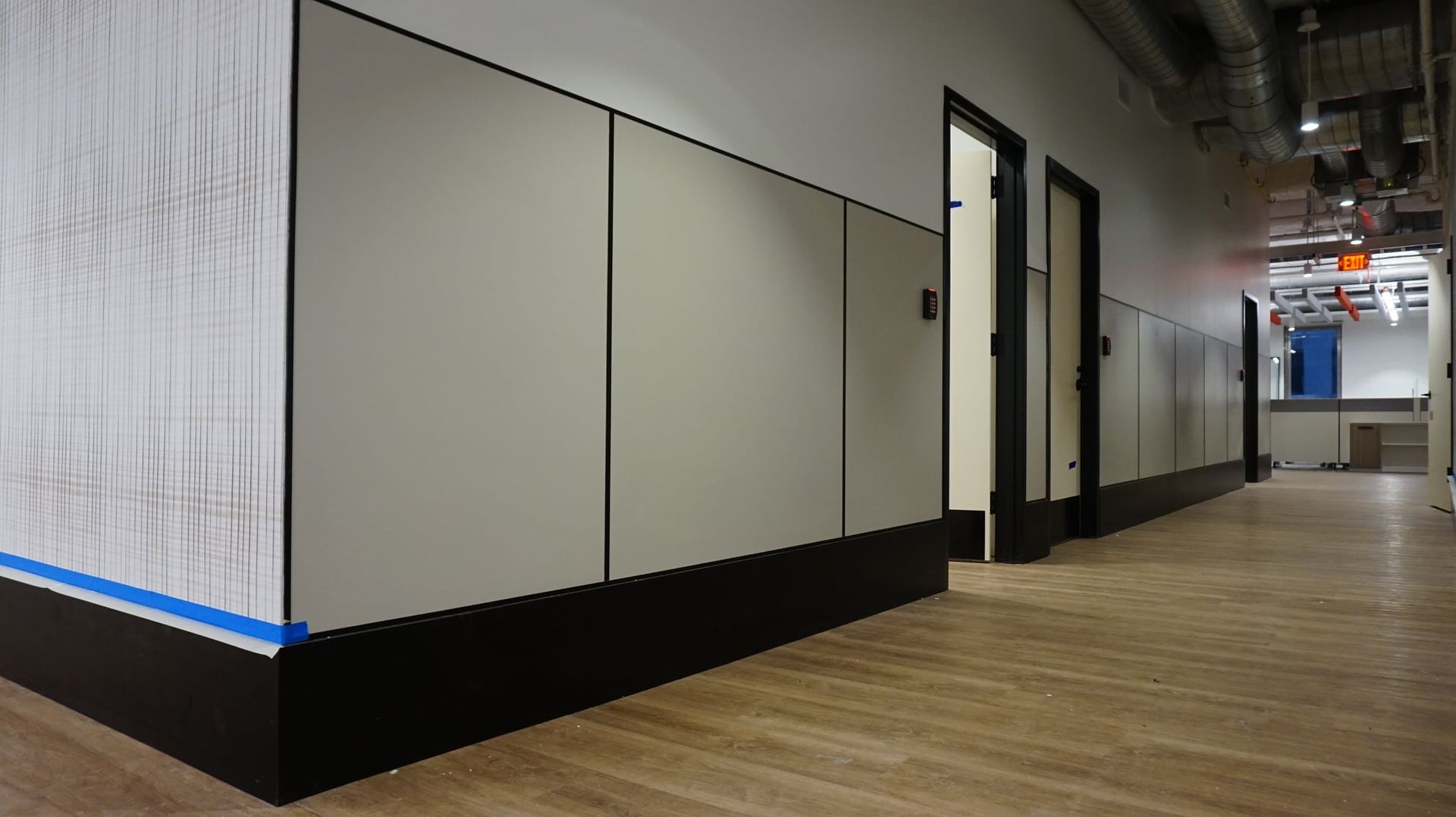 Hallway with light wood floor, white walls with gray panels, black trim and doors.