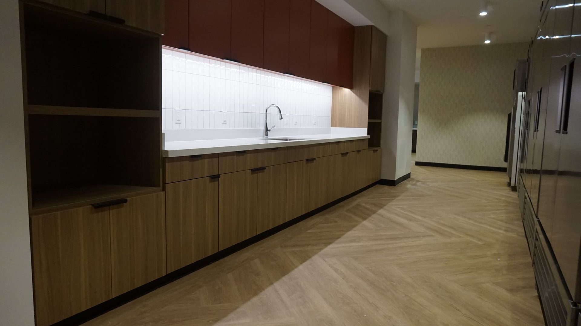 Wooden cabinets and countertop in a kitchen area with a red top cabinet and herringbone floor.