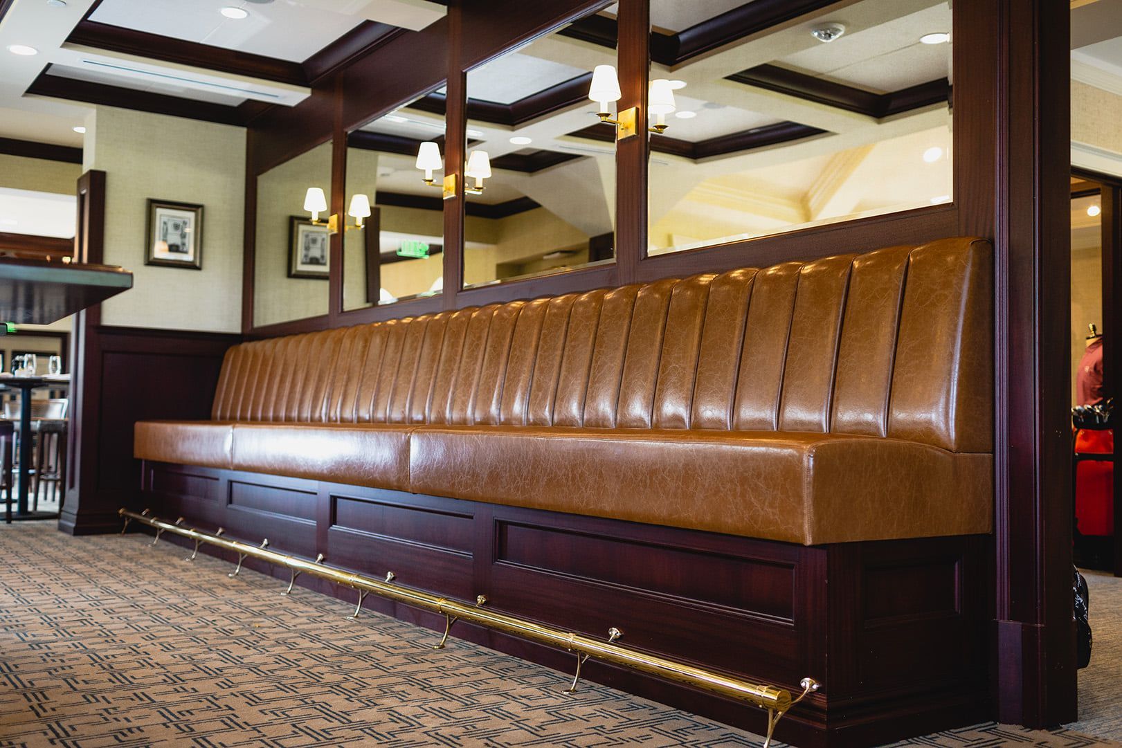 Long, brown leather booth with a brass footrest in a restaurant setting.