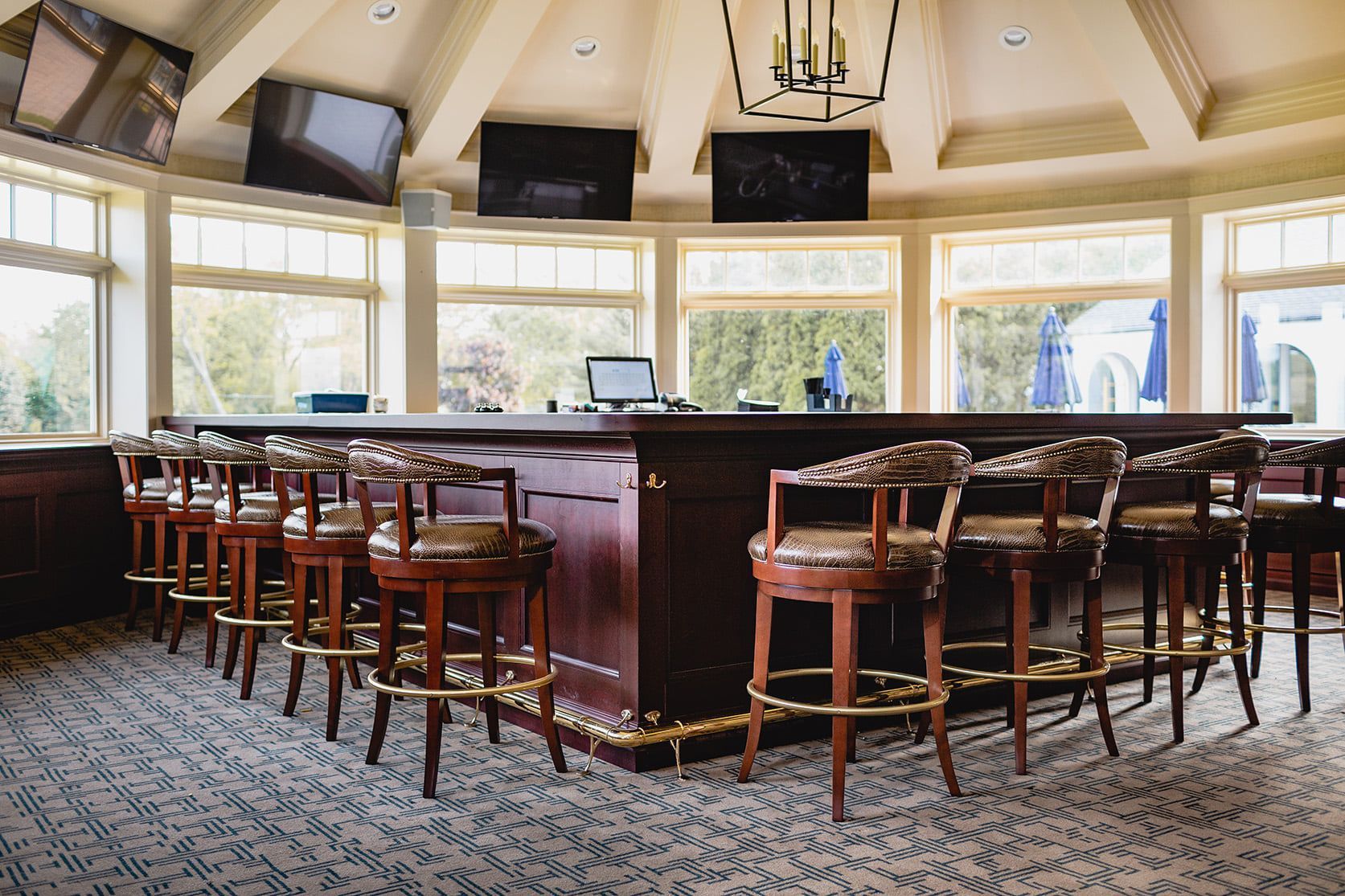 A circular bar with brown wooden stools and a dark wood bar top, surrounded by windows.