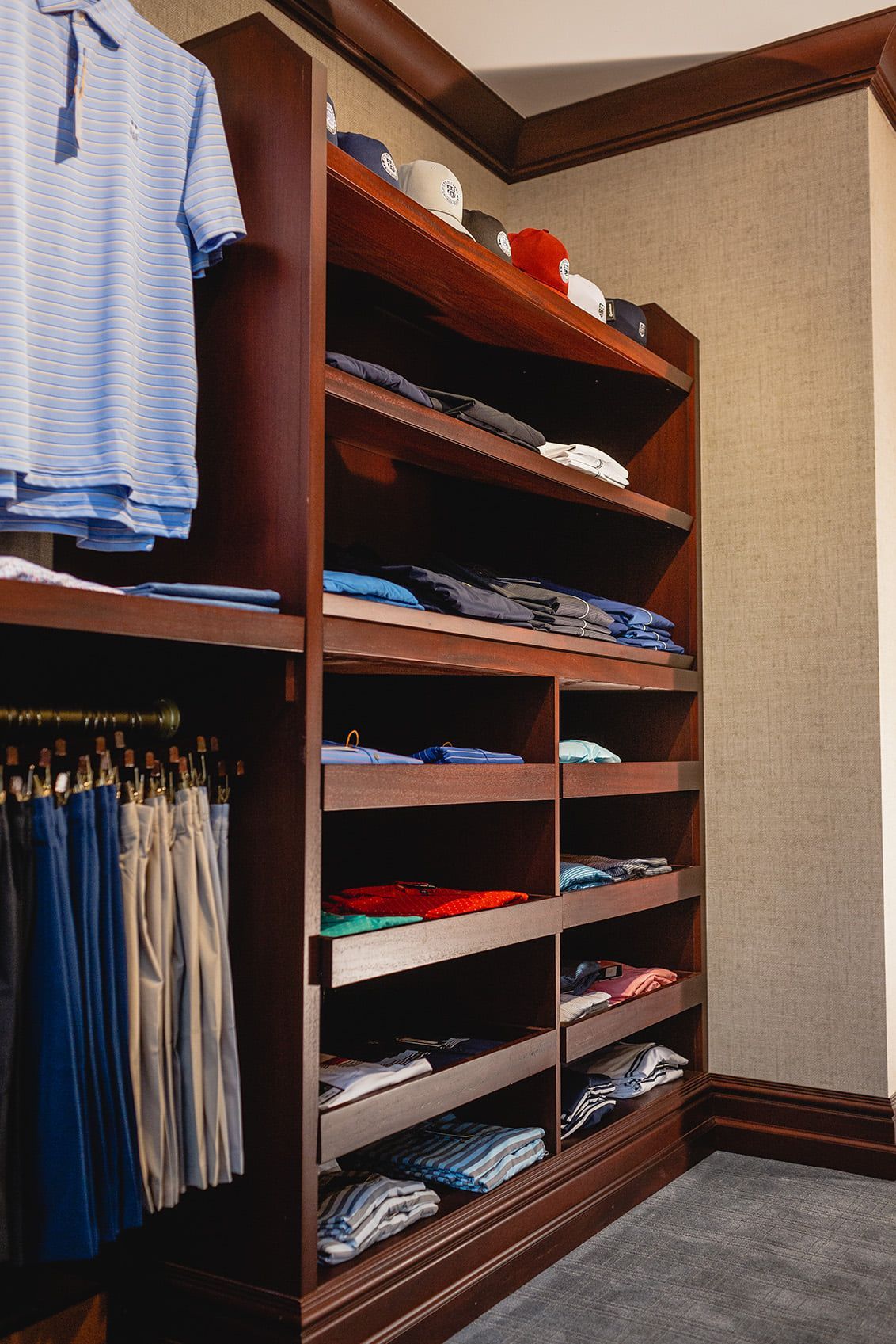 Built-in wooden closet with shelves of folded clothes, hats, and hanging shirts and pants.