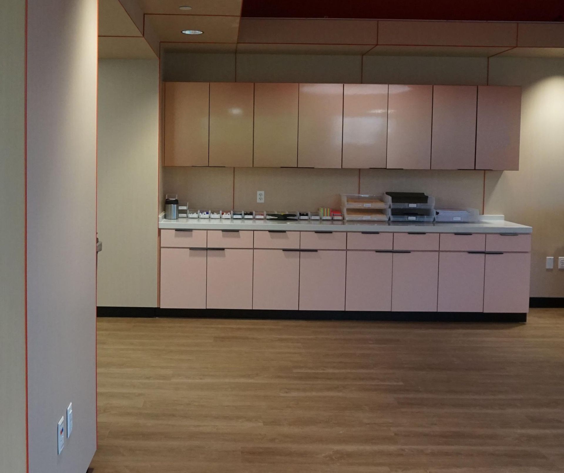 Pink kitchen cabinets with a white countertop and light brown flooring.