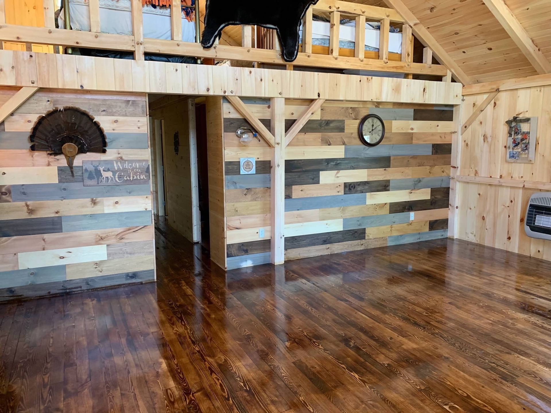 Interior of a rustic room with wood floors and walls, a loft, and mounted decorations.
