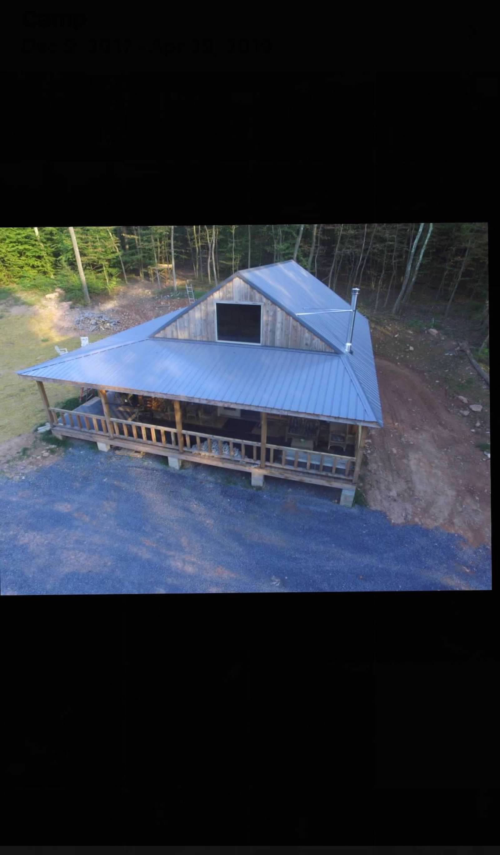 Cabin with blue metal roof and wrap-around porch in a wooded area.