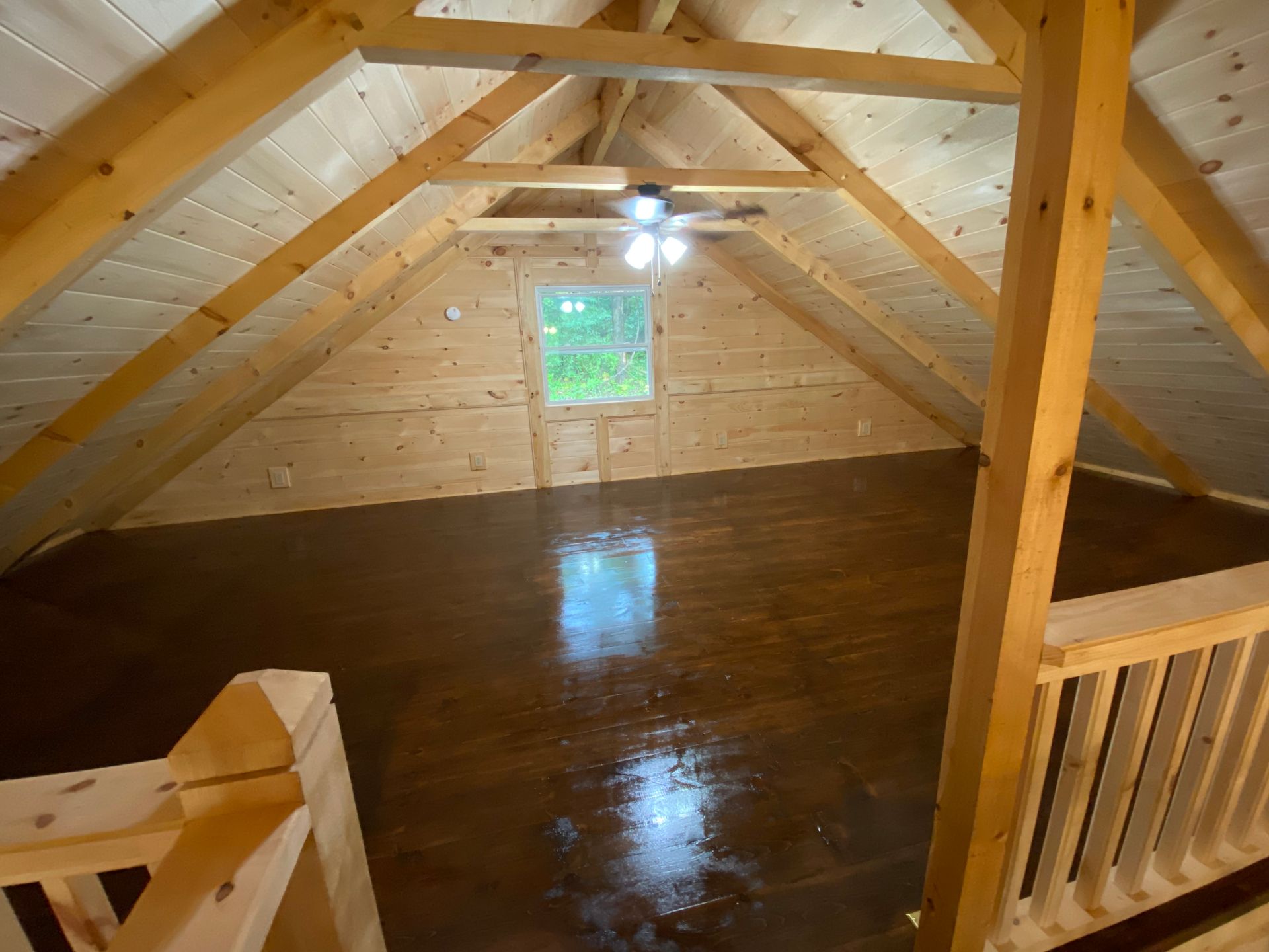 Interior of a loft space with exposed wood beams, a window, and a dark brown floor.
