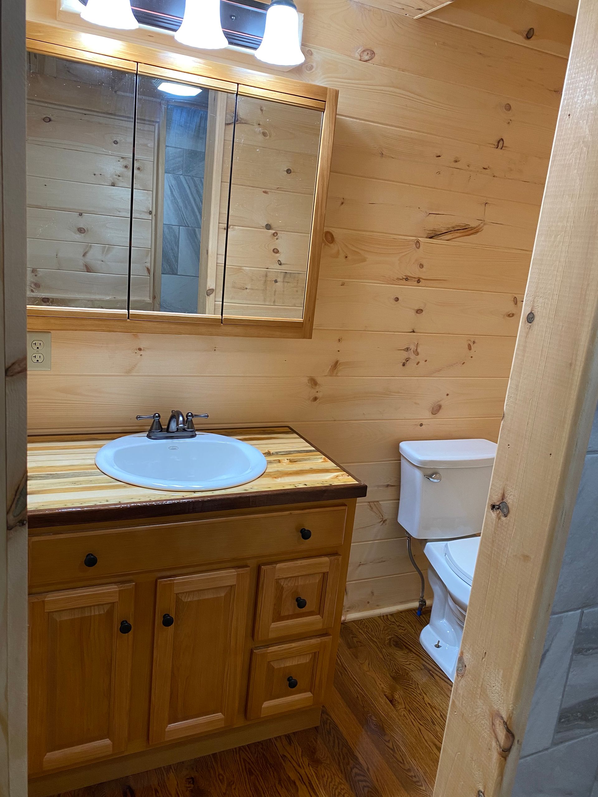 Bathroom with wooden walls, vanity, mirror, and toilet.