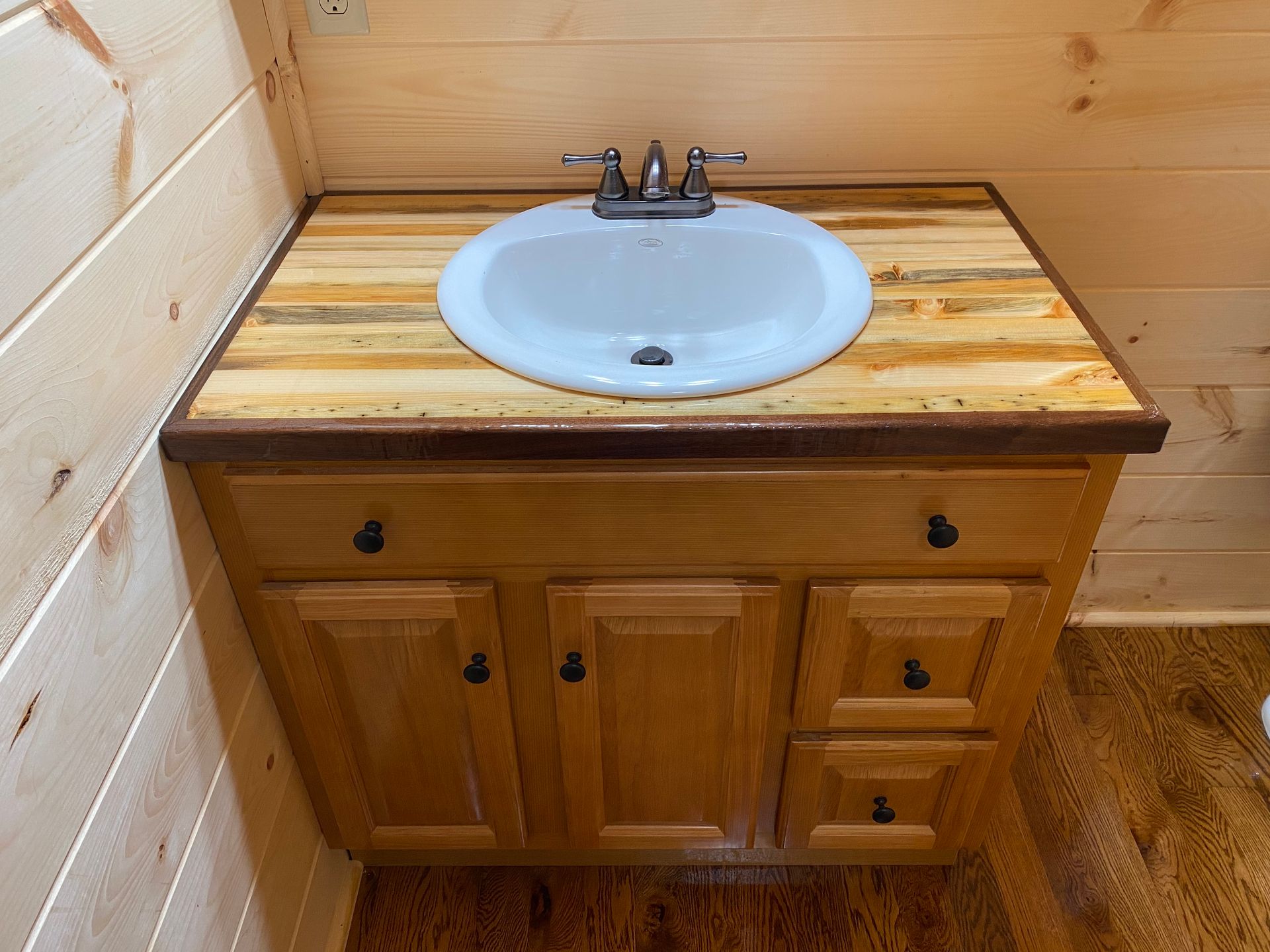 Bathroom vanity with light wood cabinet, wood countertop, white sink, and chrome faucet.
