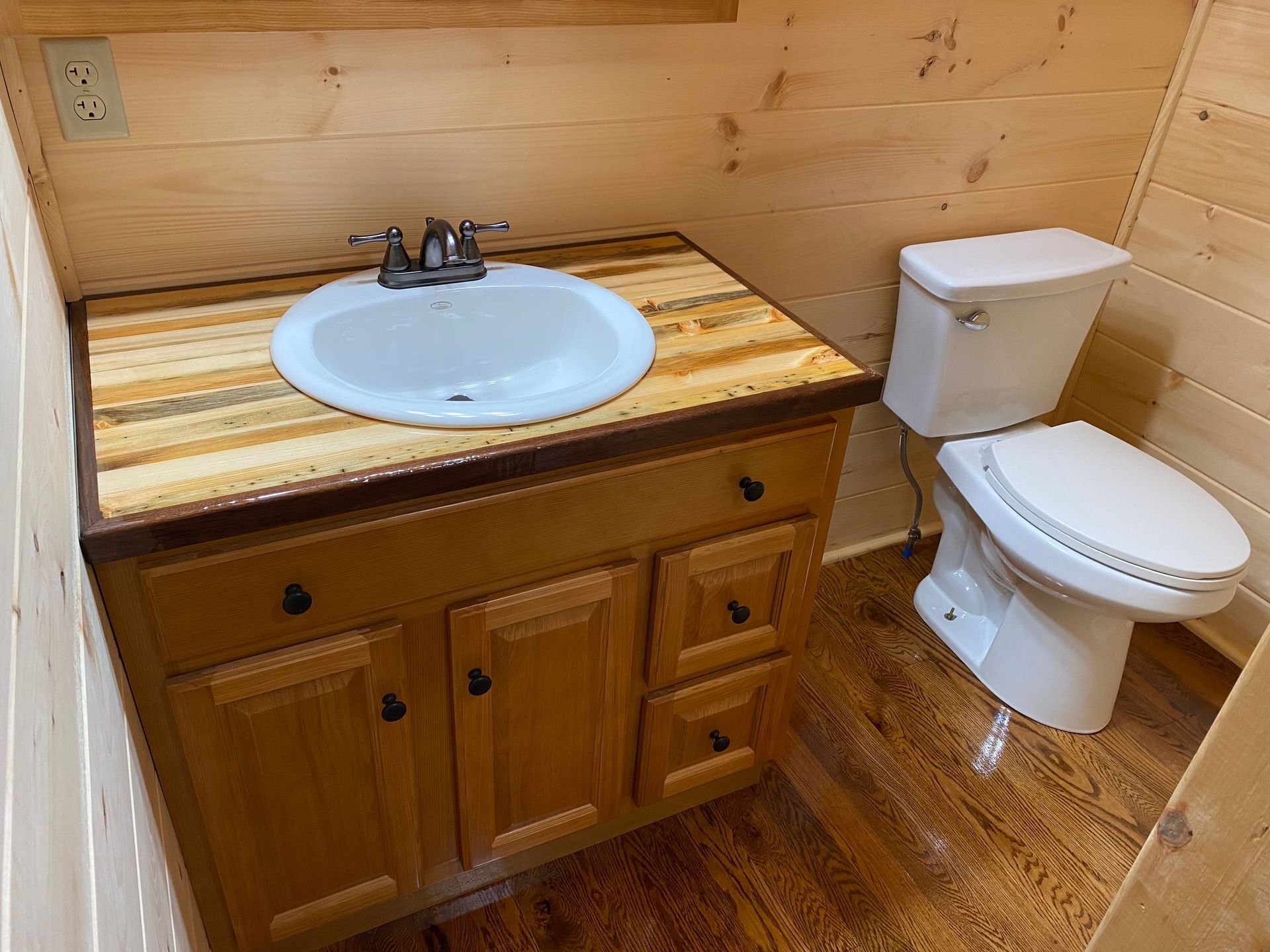 Bathroom with a sink, vanity, and toilet; light wood paneling and flooring.