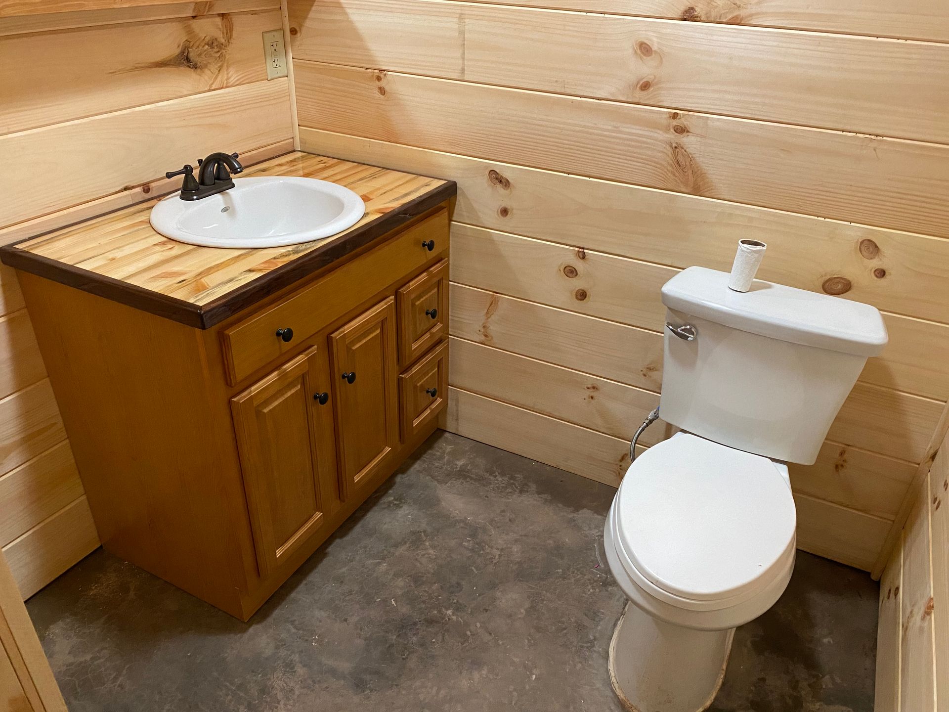 Bathroom with a wood vanity, sink, and toilet; light-colored wood paneling on the walls.