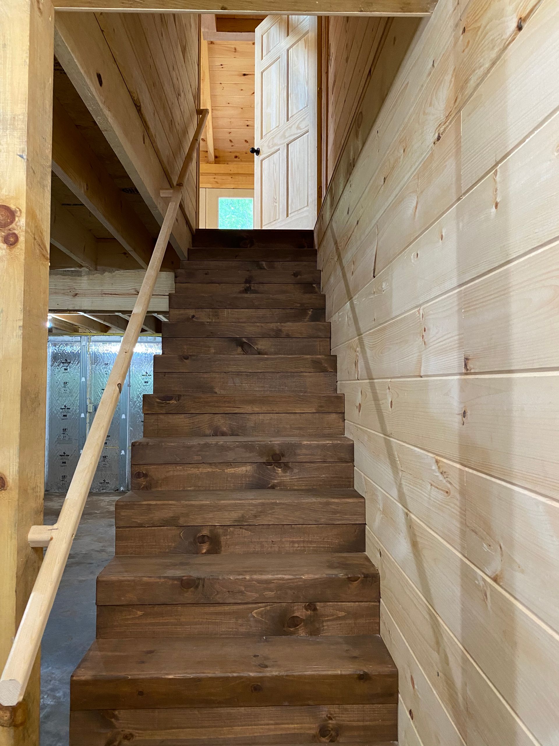 Wooden staircase leading upwards to a door. Handrail on left, wood-paneled walls on right.
