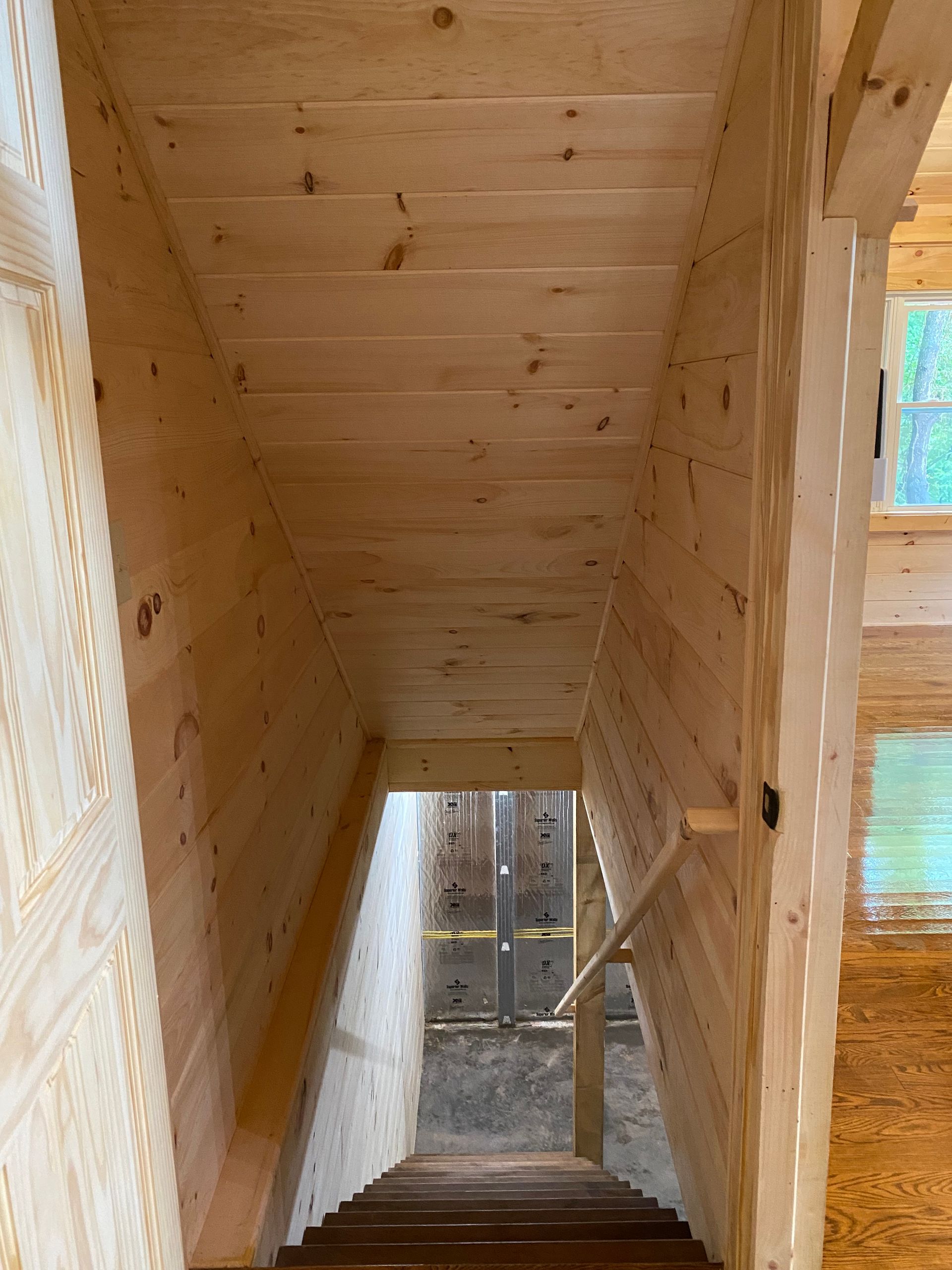 Wooden staircase leading downwards, walls and ceiling also wood. Railing on the right.