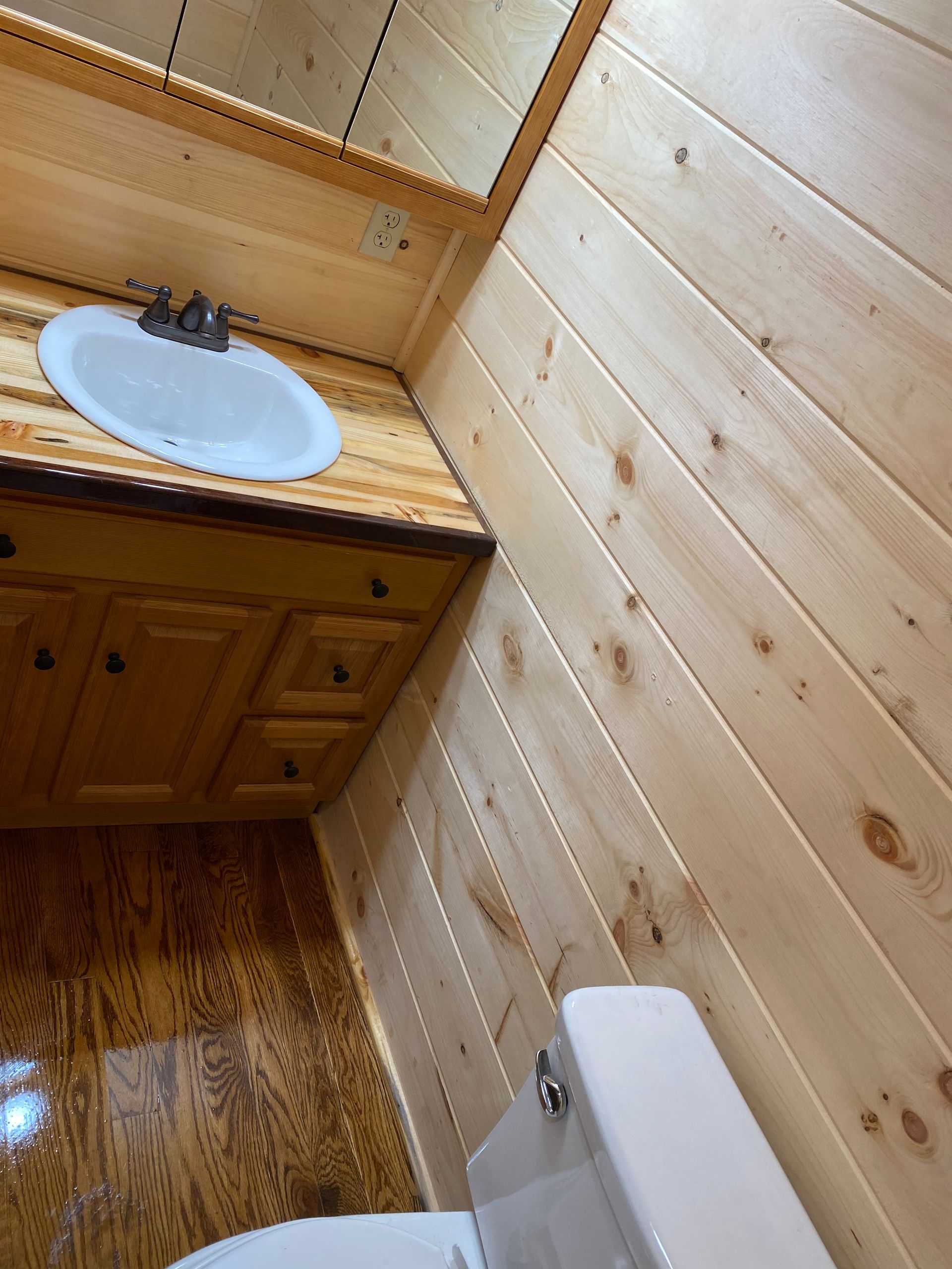 Bathroom with wood paneling on walls, vanity, and floor. White sink and toilet.