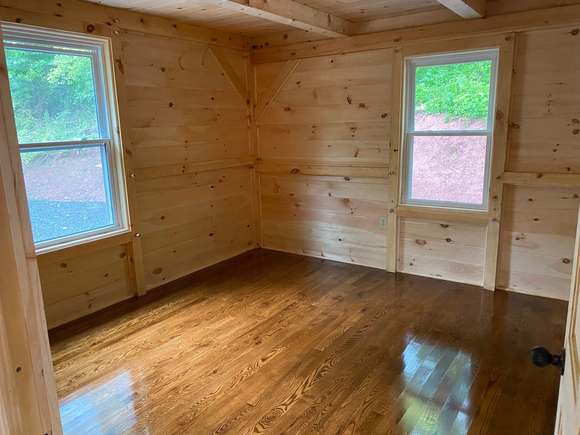 Empty room with wood walls and floor, two windows.