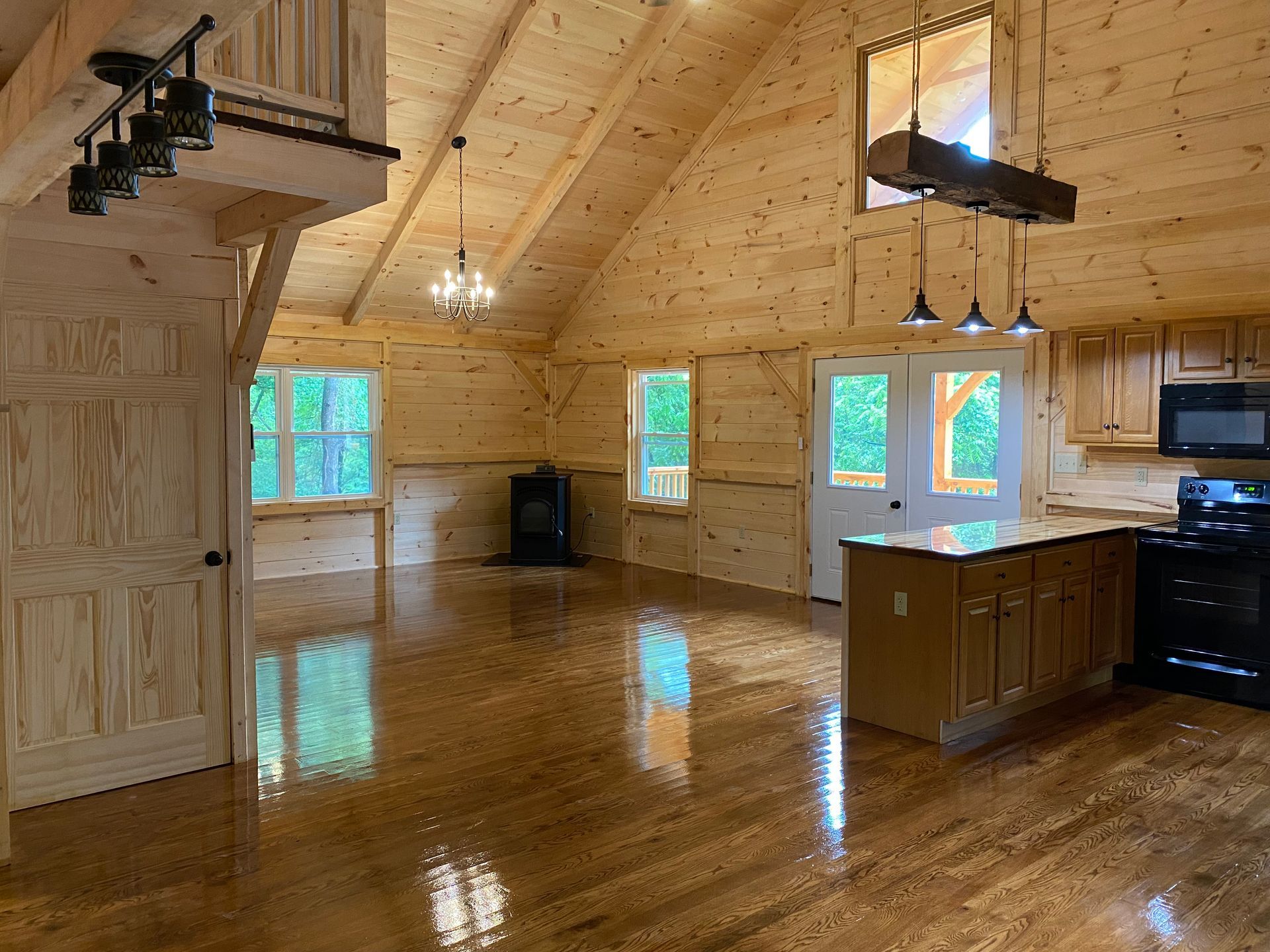 Interior of a wood-paneled cabin. Kitchen with island and appliances; stairs lead to a loft.
