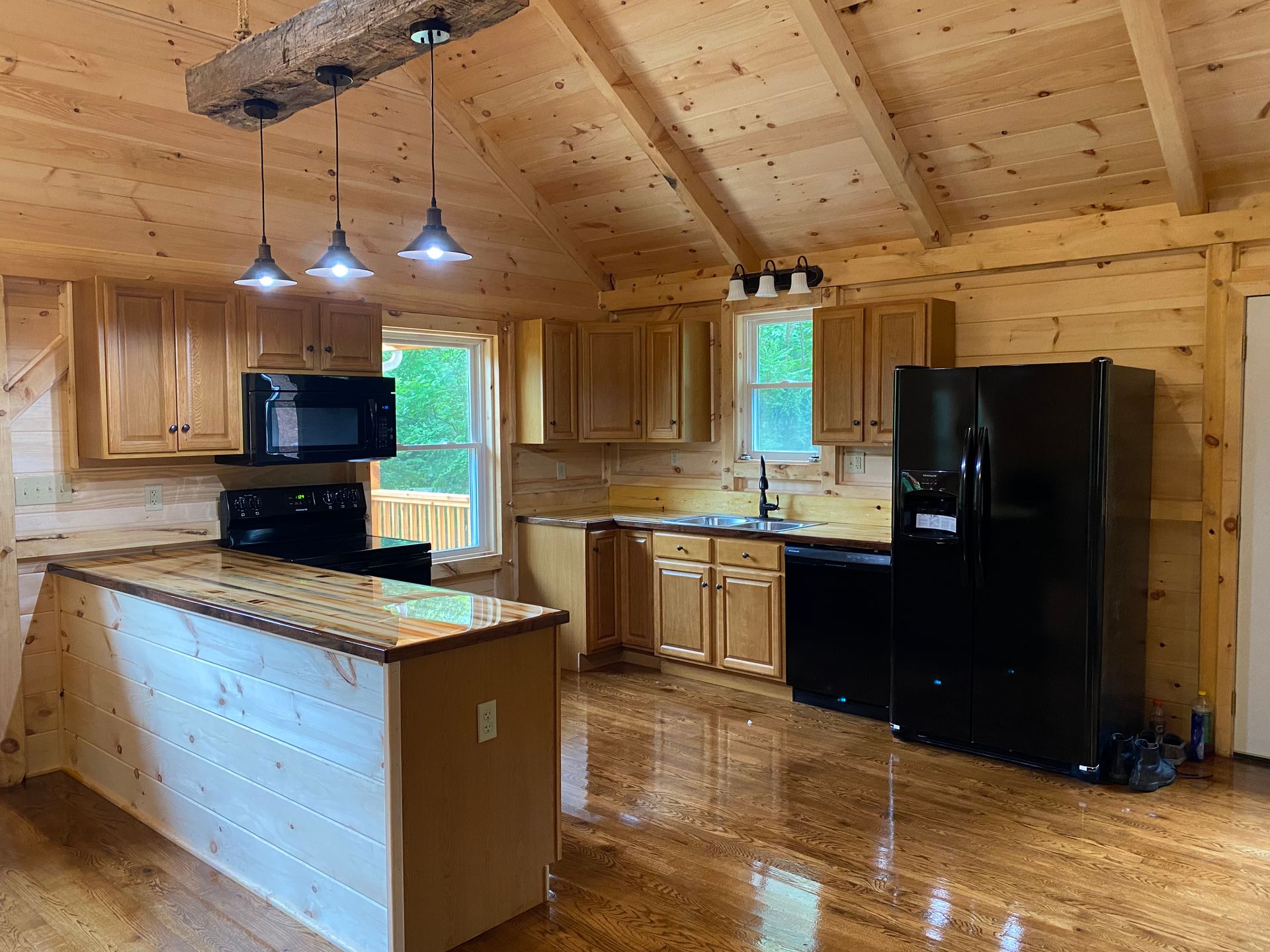 Kitchen with light wood cabinets, black appliances, and pendant lights.