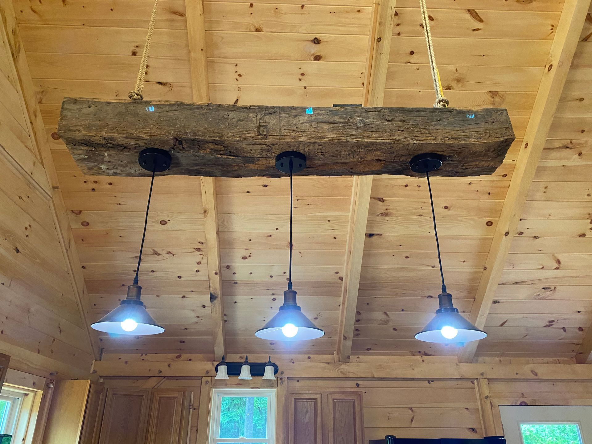 Rustic wooden beam light fixture with three pendant lights hanging from a wood ceiling.