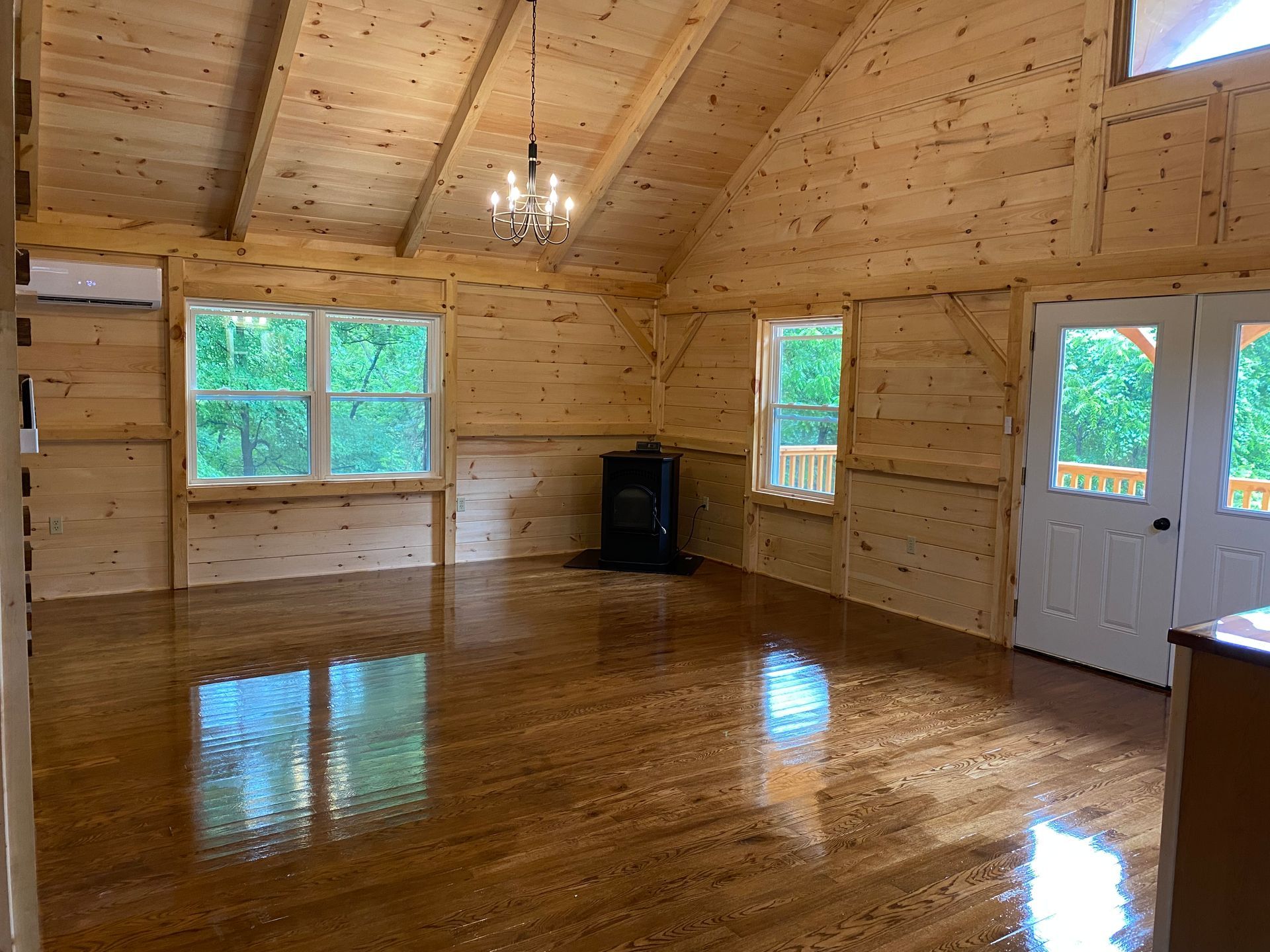 Interior view of a cabin with wood walls and floors, windows, and a chandelier.