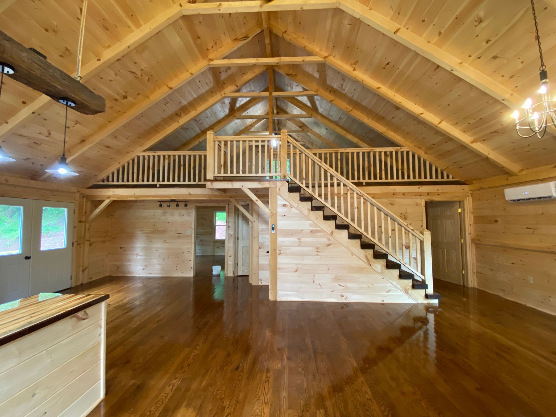 Interior of a wooden cabin with a loft and staircase, featuring hardwood floors and exposed beams.