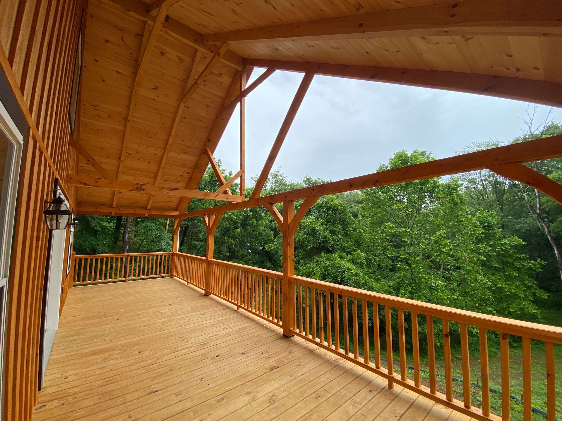 Wooden covered porch with railing overlooking trees.