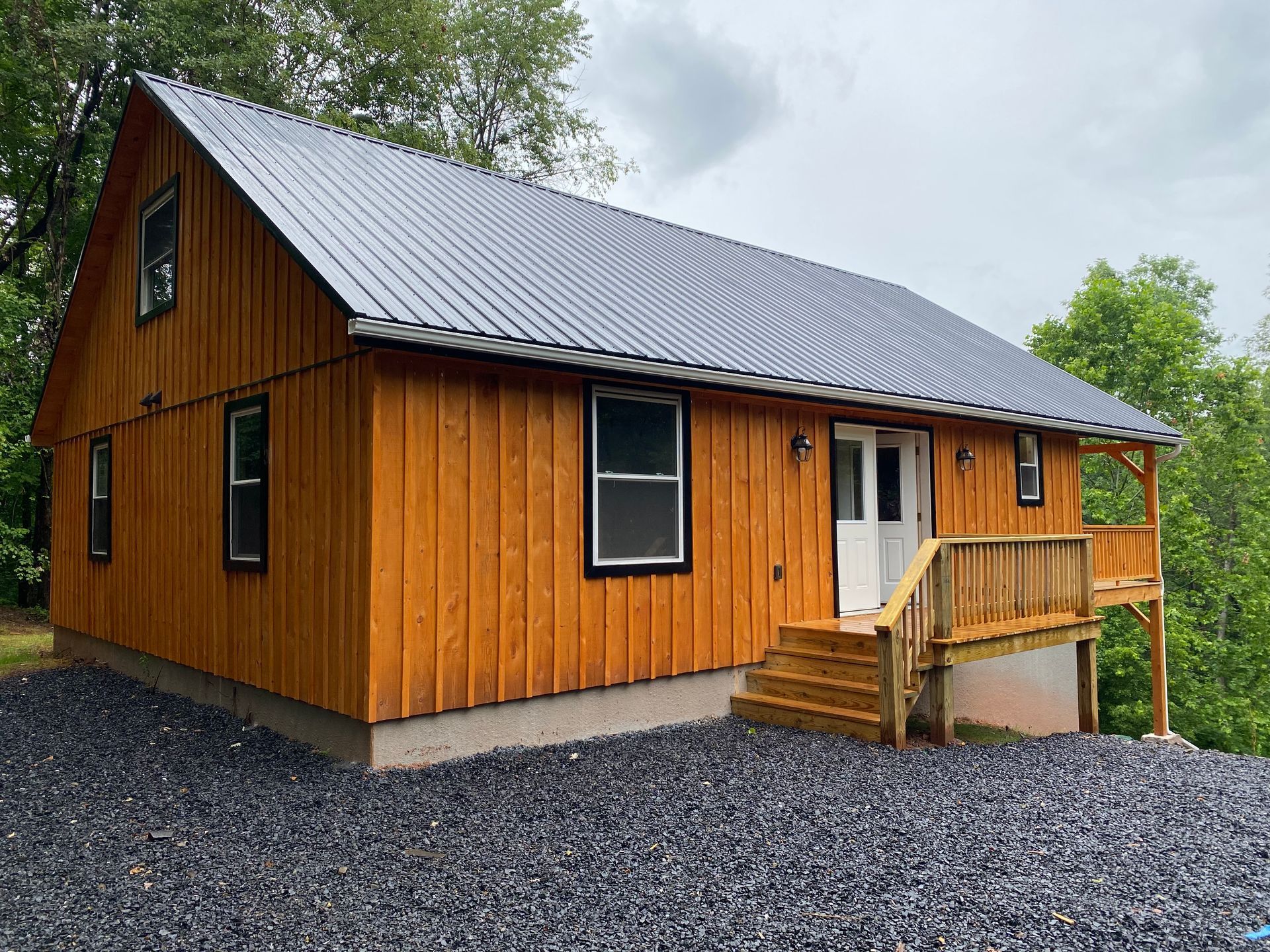Wooden cabin with a dark gray roof, windows with black frames, and a small porch.