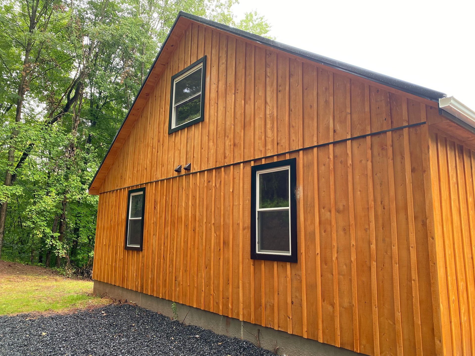 Wooden building with black-framed windows and dark trim, set against a backdrop of trees.