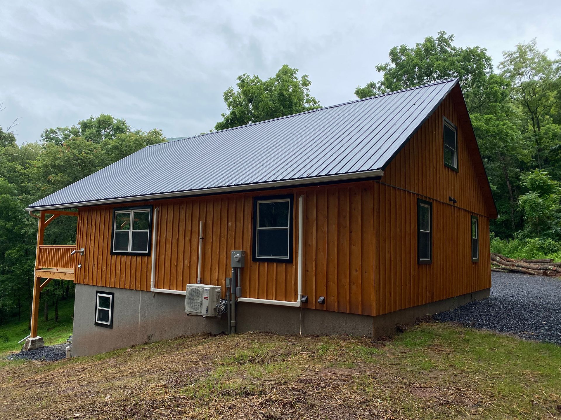 Wooden cabin with metal roof, set on a slight hill, surrounded by trees.