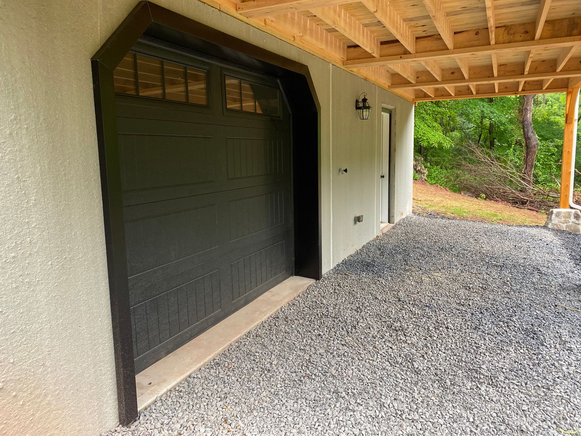 Black garage door and gravel driveway under a wooden porch.