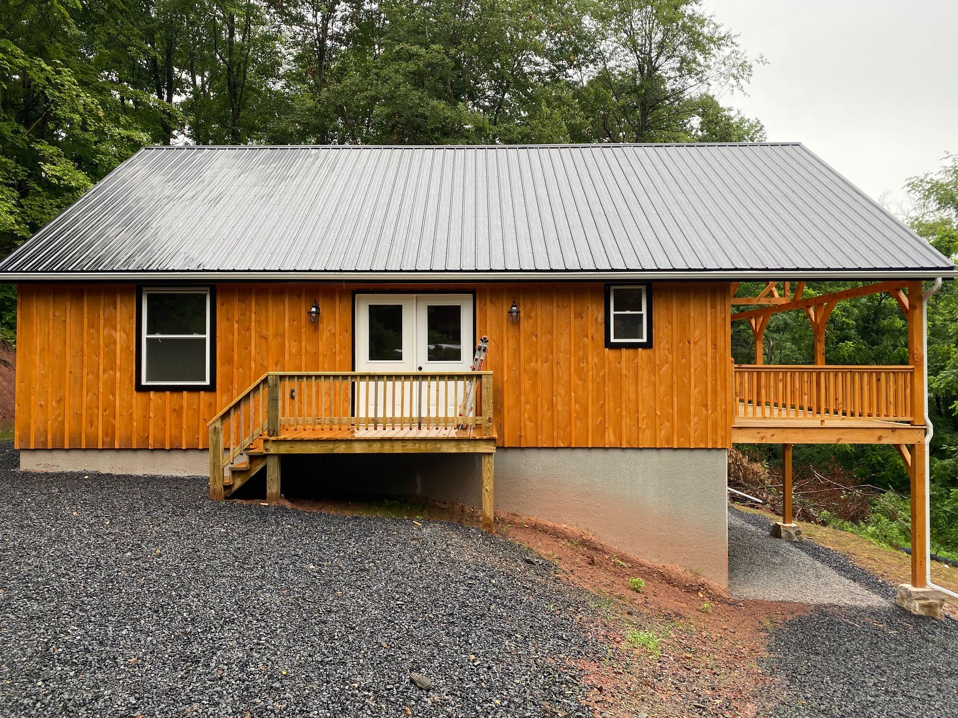Cabin with a metal roof, wooden siding, and a small deck. Located on a gravel hill.