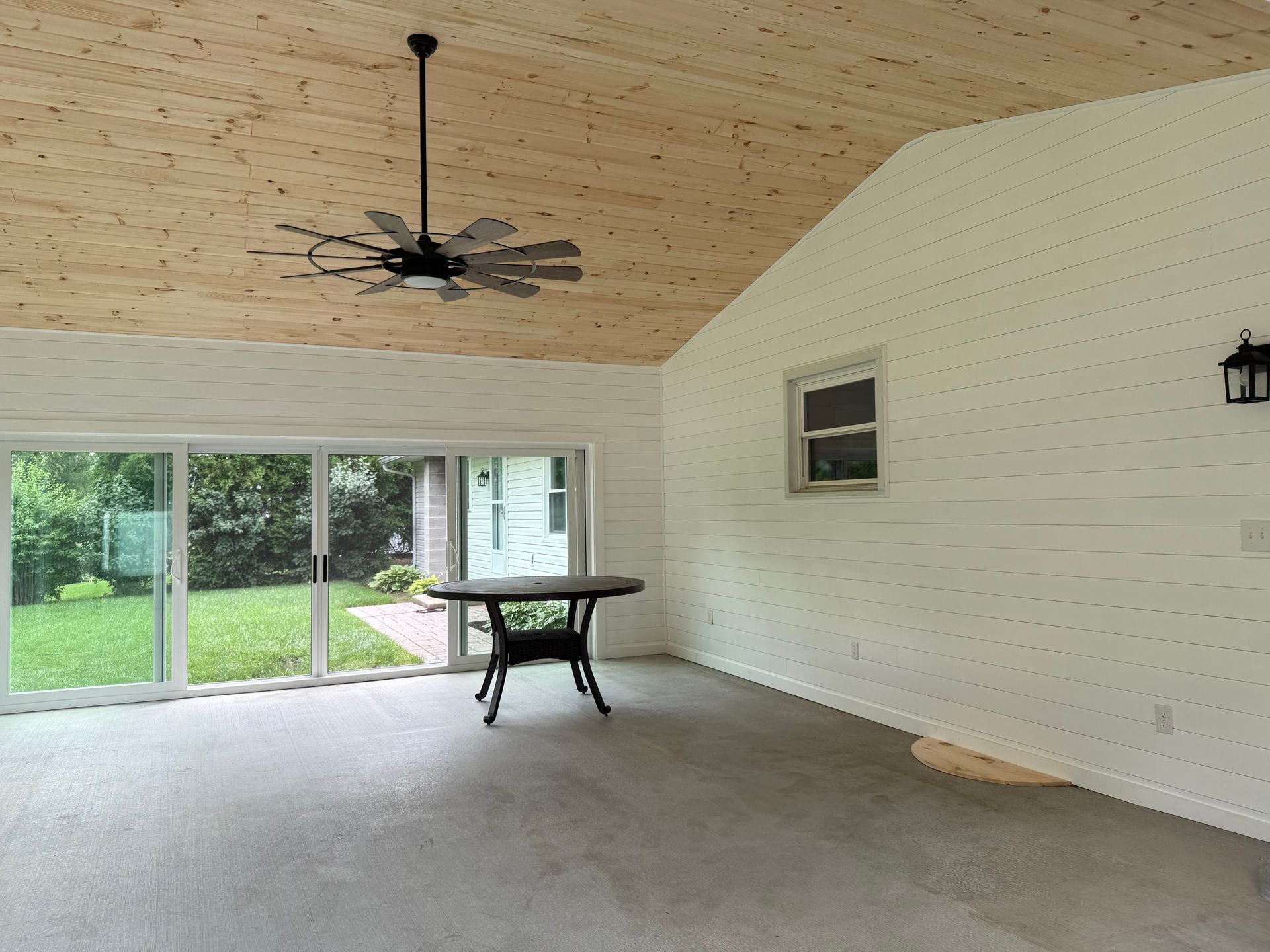 A room with a wood ceiling, white walls, gray carpet, and a sliding glass door.