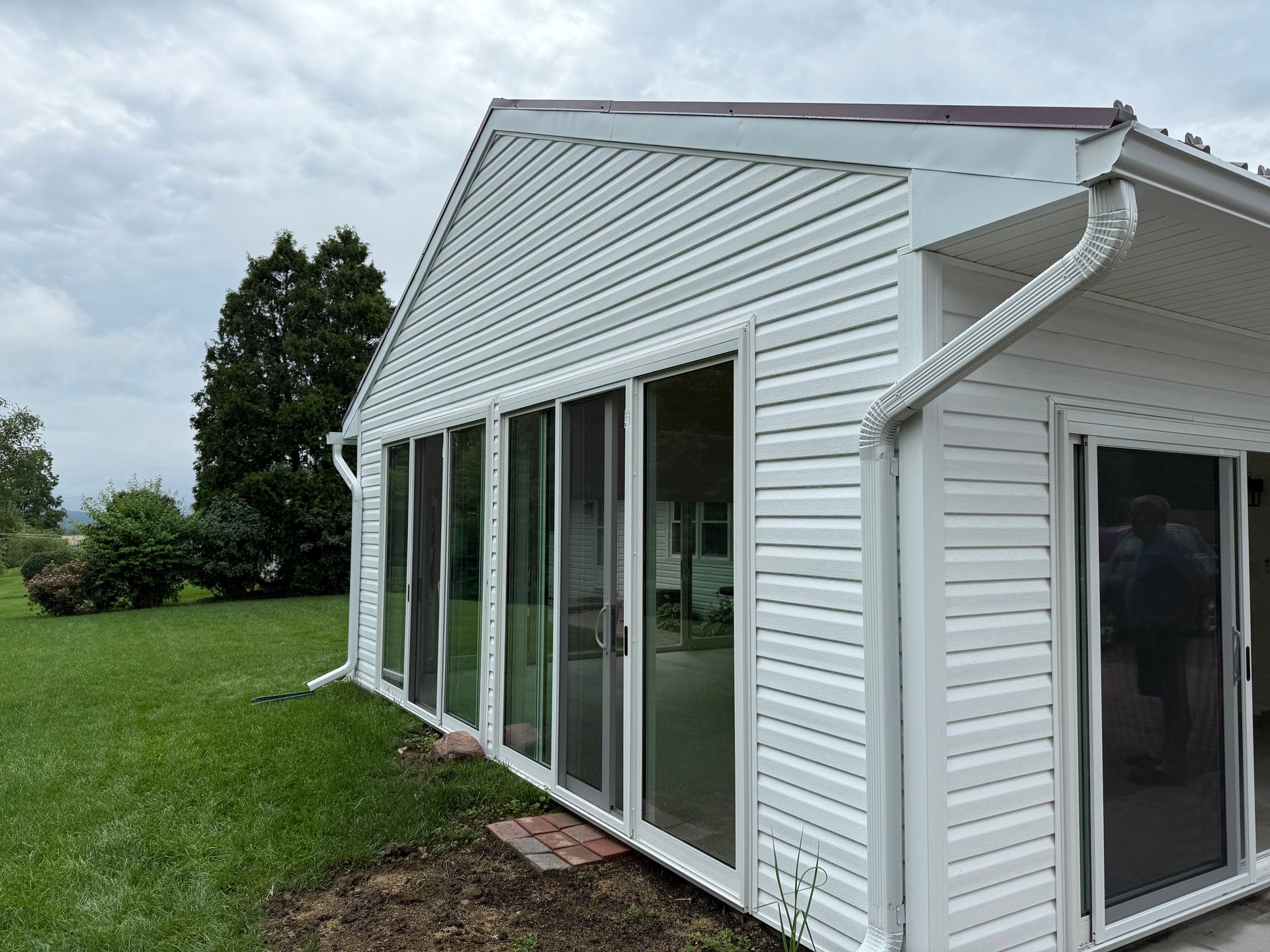 White siding and glass-walled sunroom on a grassy lawn under a cloudy sky.