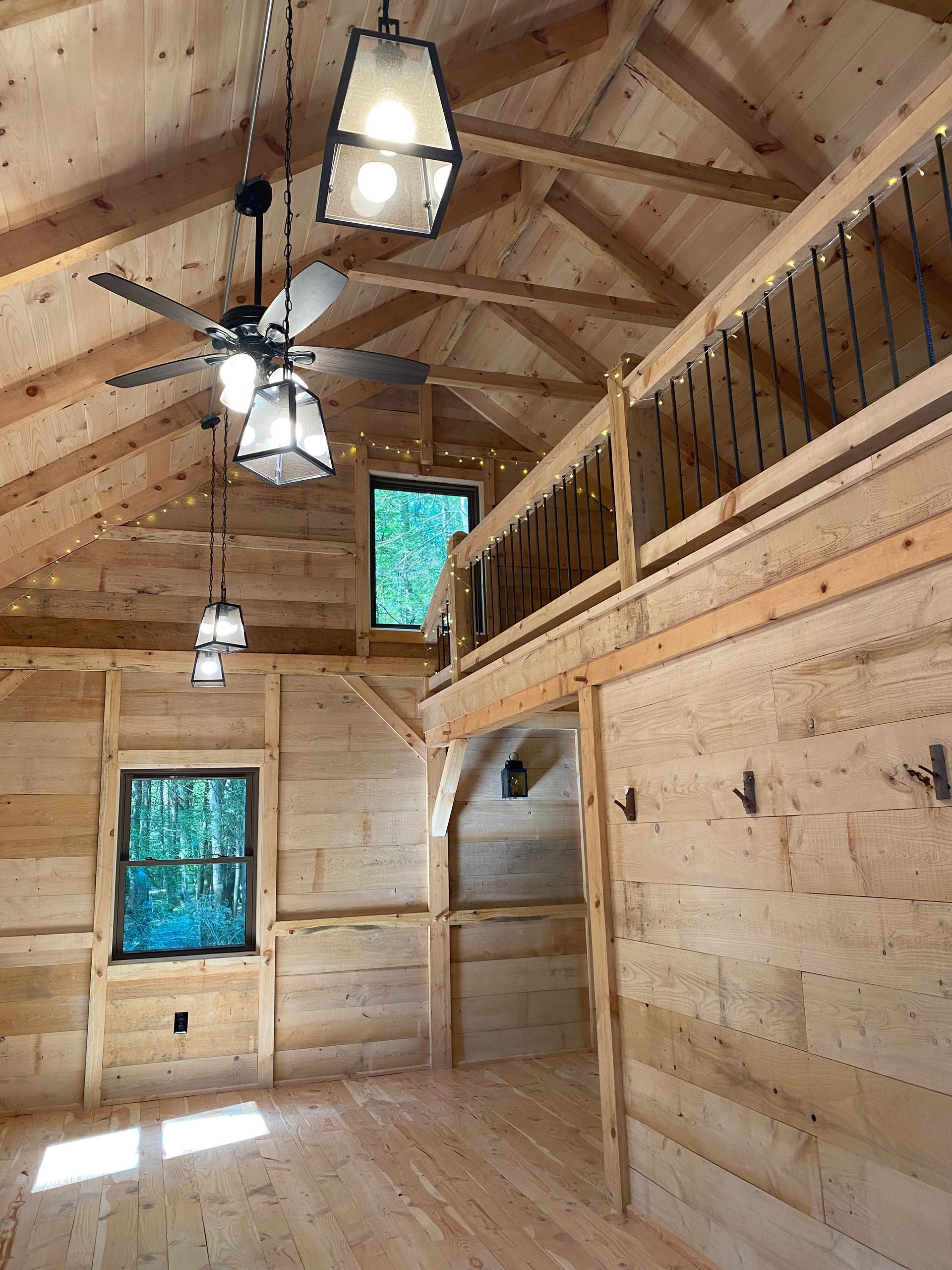 Interior of a rustic wooden cabin with a loft, windows, and hanging lights.